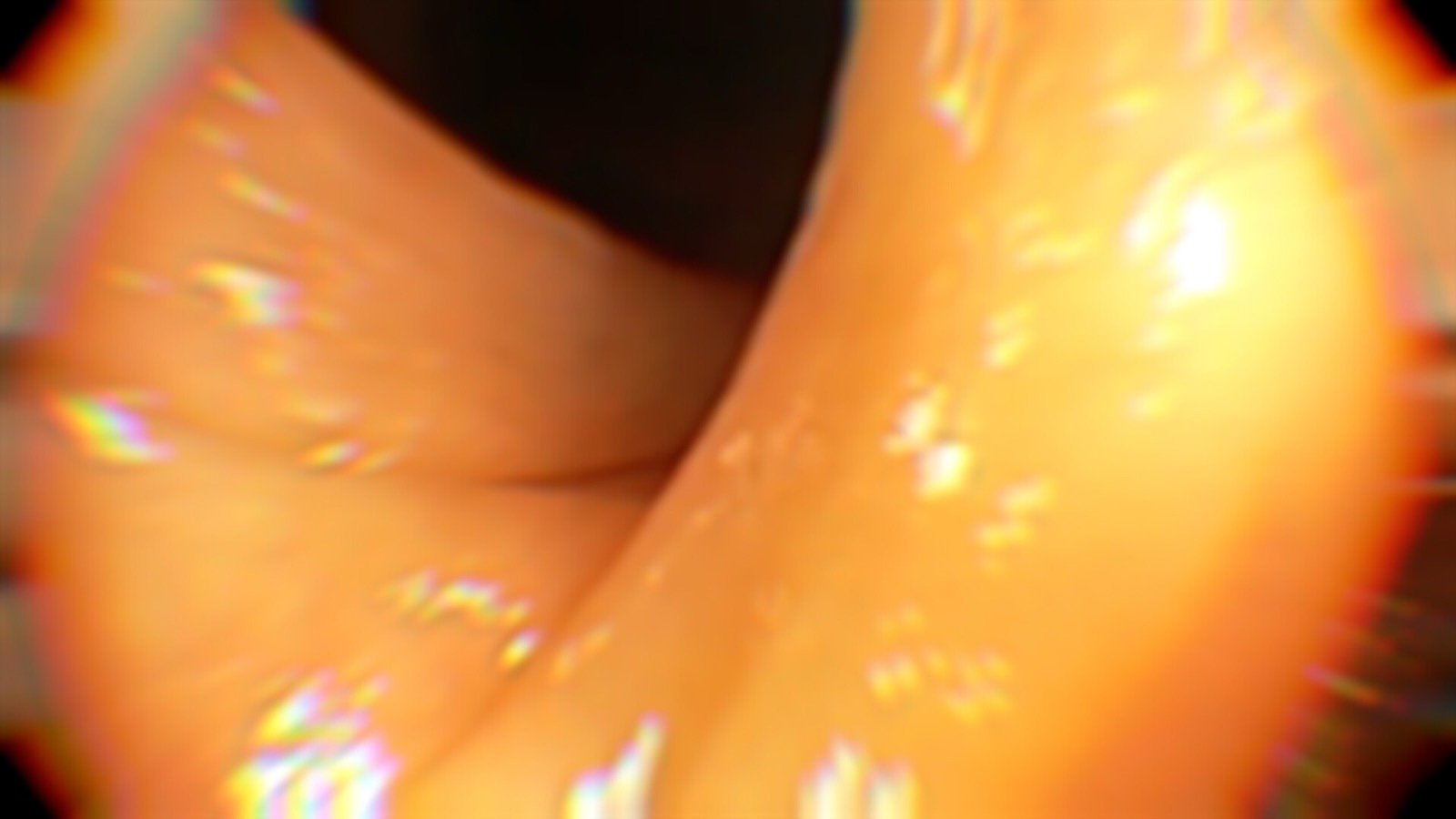 Abstract close-up of skin-toned forms with warm, blurred lighting and reflective highlights.