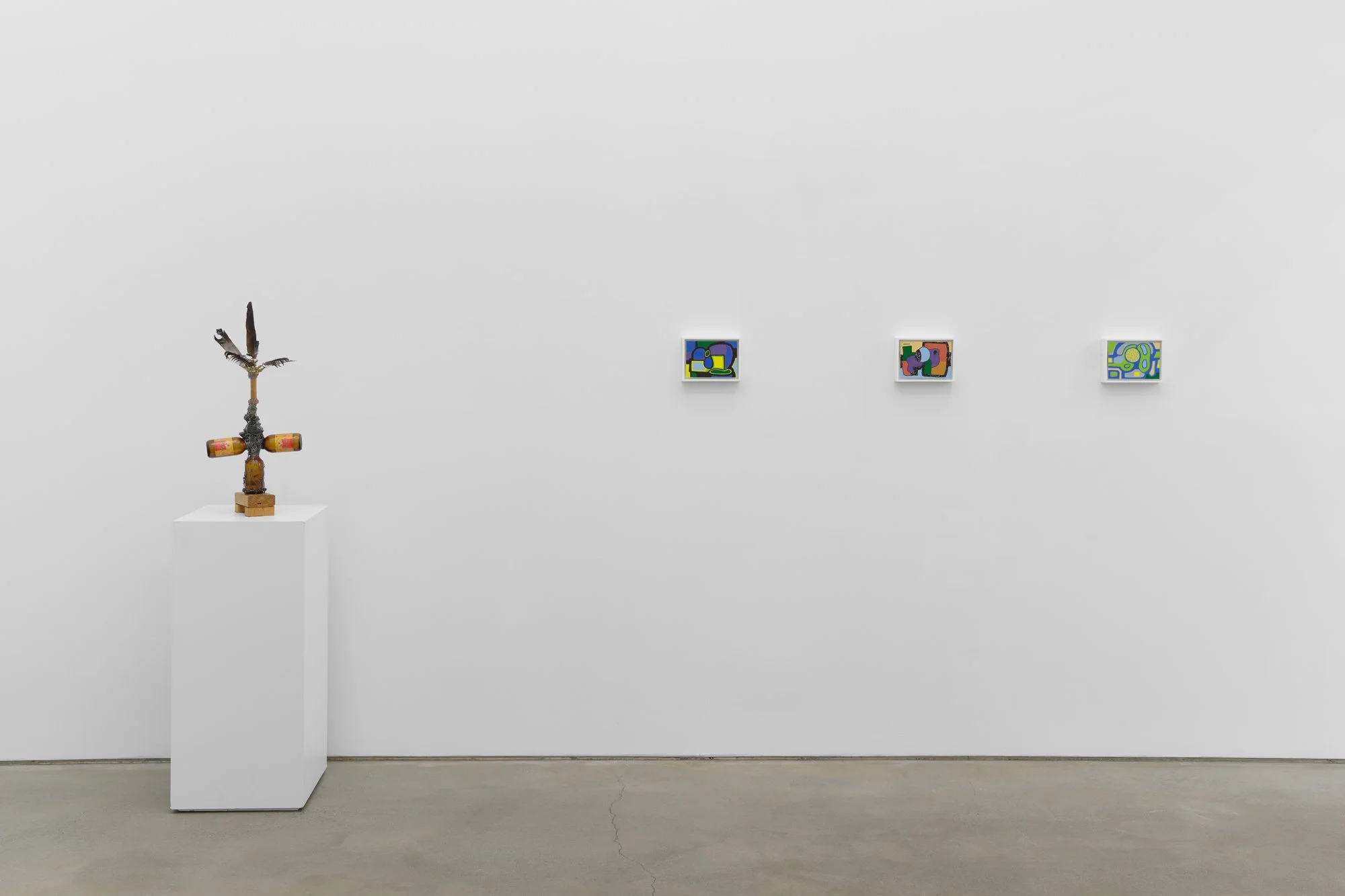 Minimal gallery wall with a small sculptural object on a pedestal and three colorful abstract paintings hung in a row.