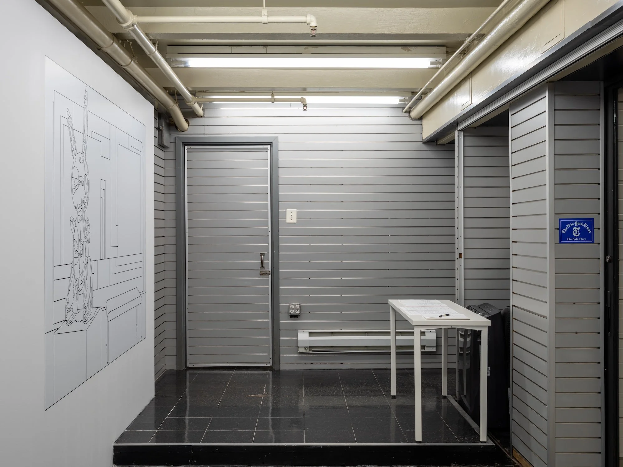 Interior gallery space showing a large wall drawing of a rabbit sculpture, with a white table and sign-in sheet nearby.