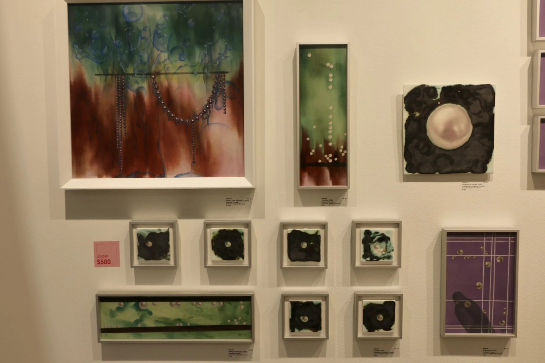 Gallery wall displaying colorful abstract paintings and small framed works, arranged salon-style.