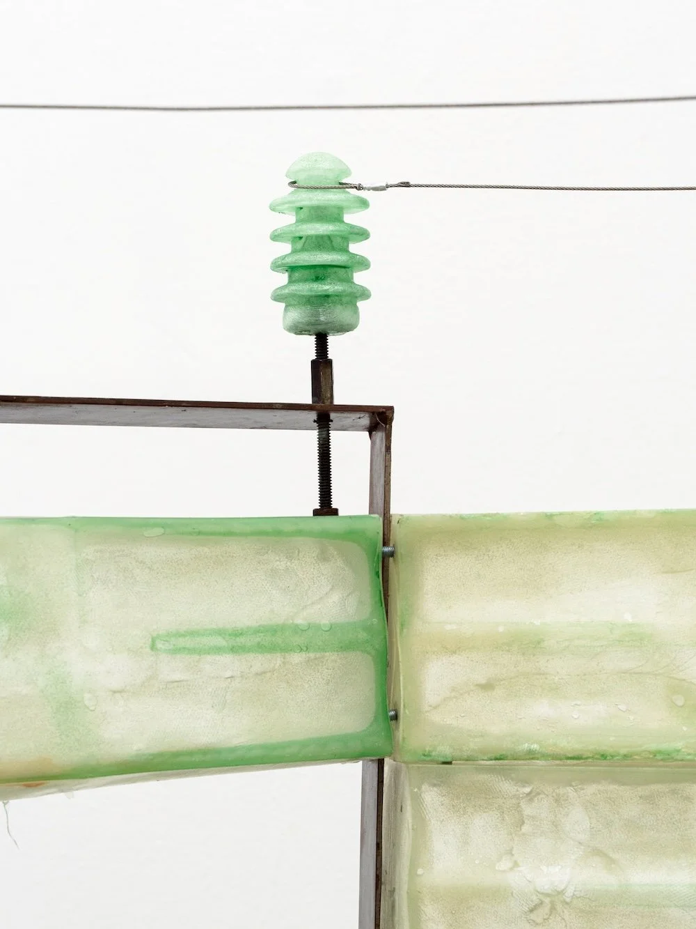 Translucent green resin structure with metal brackets and a small glass insulator connected to a taut wire.