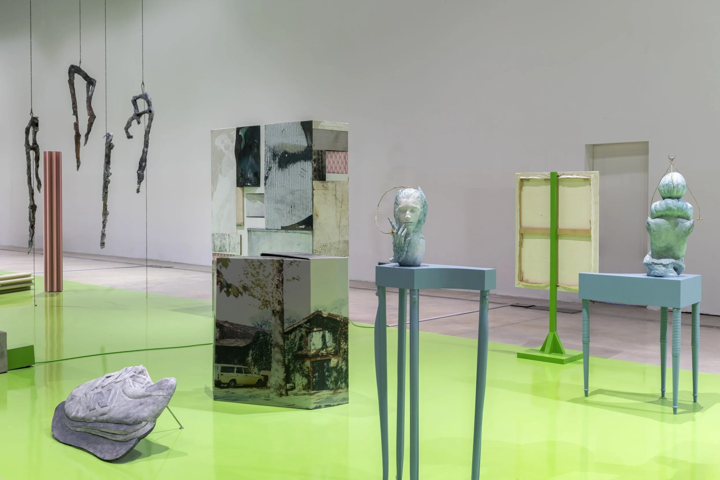 A large white room with partial green flooring hosts a number of sculptures, each visually distinct.
