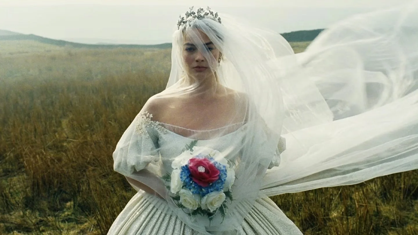 A woman dressed in an elaborate, puffy white dress and veil, holding a bouquet of flowers, centrally faces the camera. Behind her is a sprawling, grassy moor.