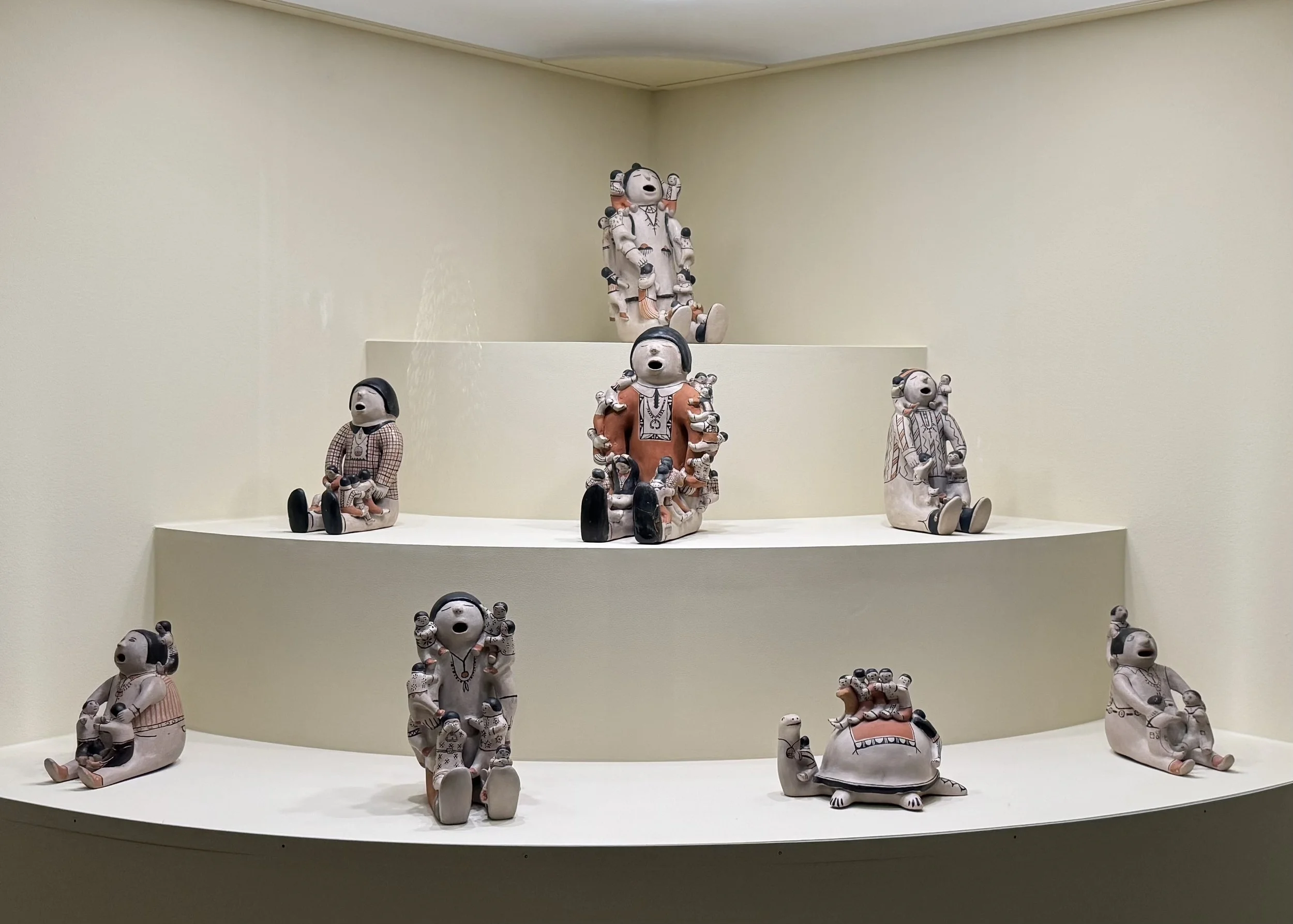 Tiered display of ceramic figures seated with open mouths, arranged in a curved wall niche.