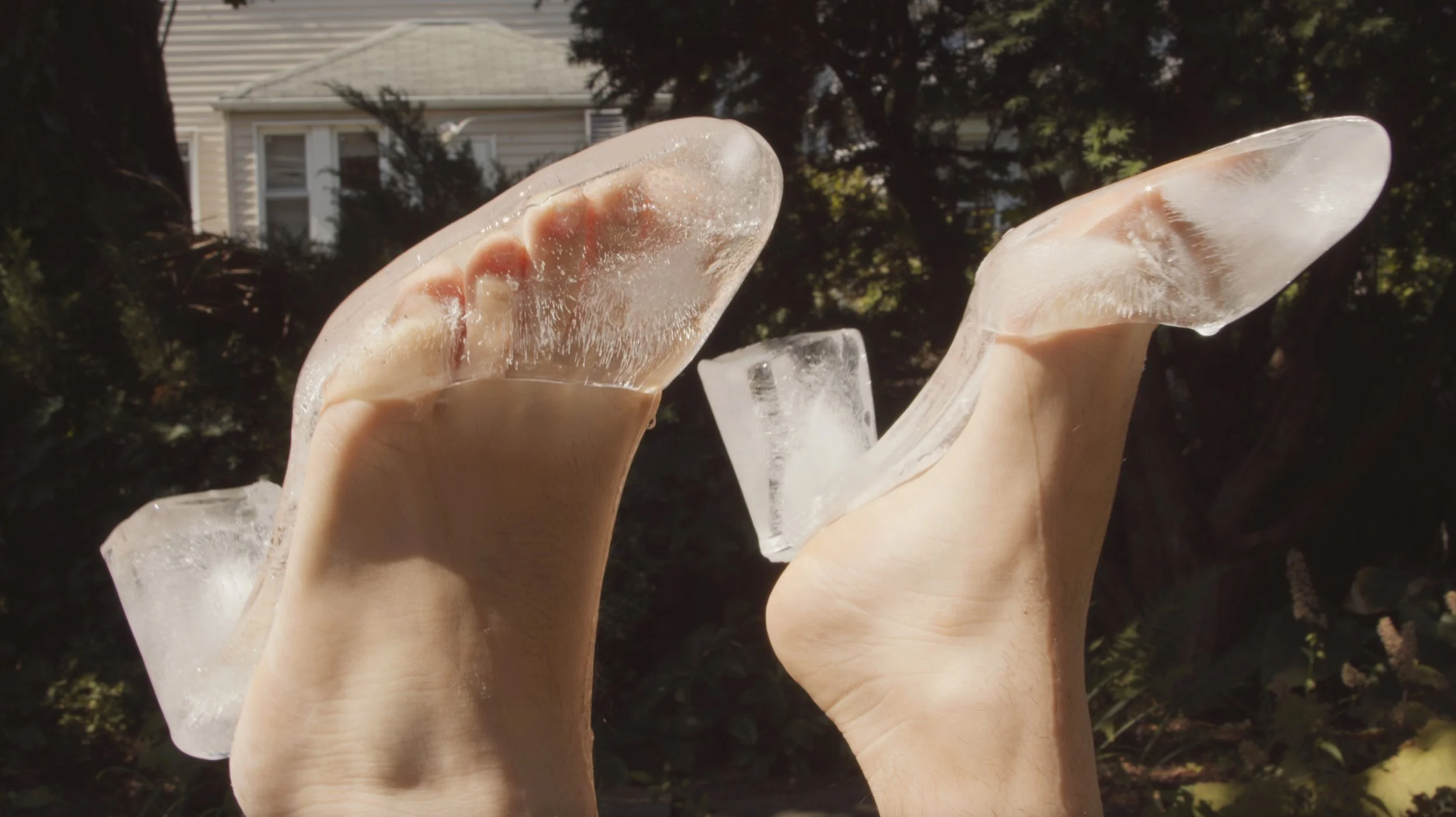 Two feet raised in the air wear heels made out of ice. Water drips from the melting ice shoes.