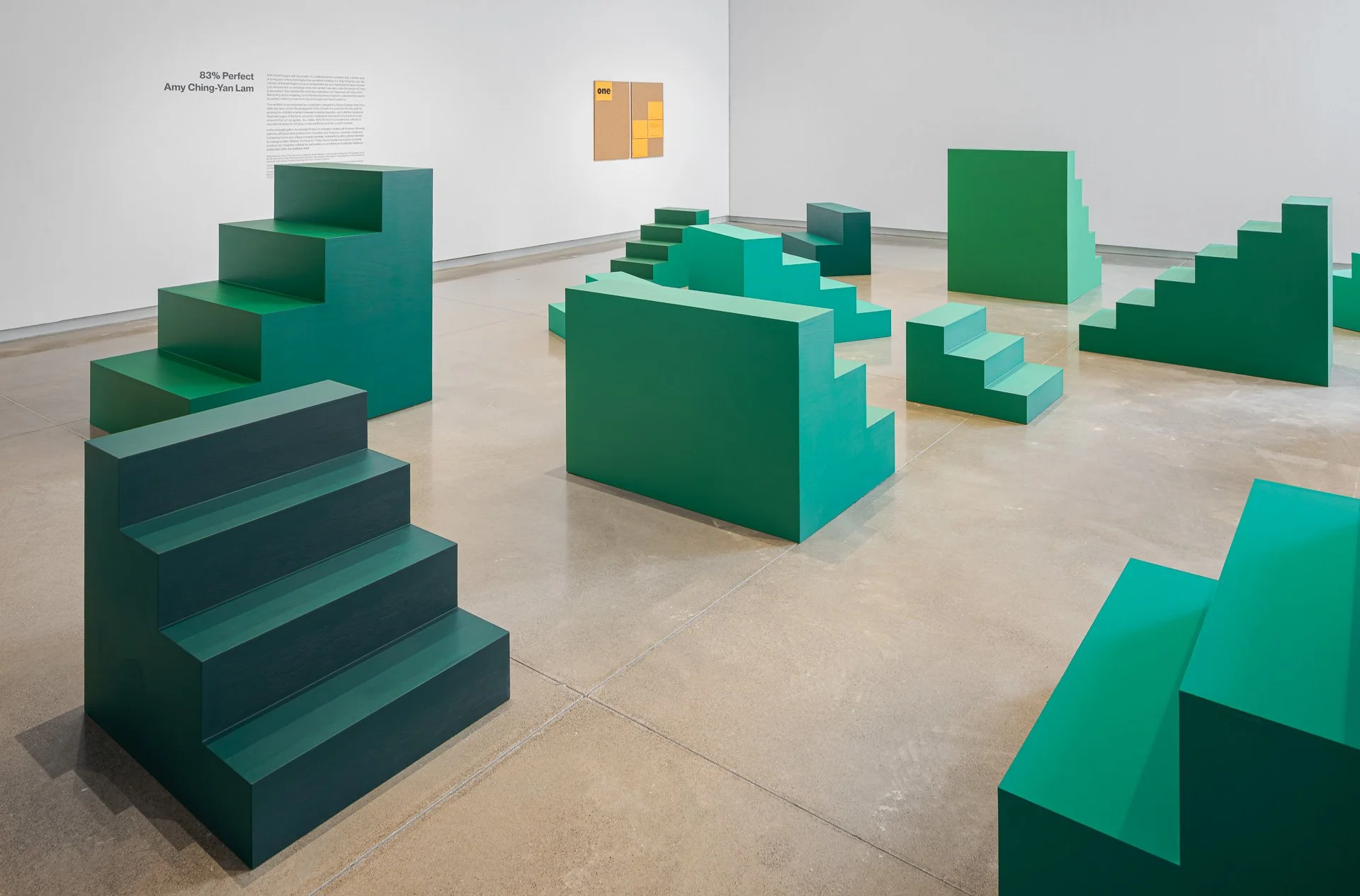 A white gallery room is populated by man short green staircases that stop at knee, hip, and shoulder length, all facing different directions.