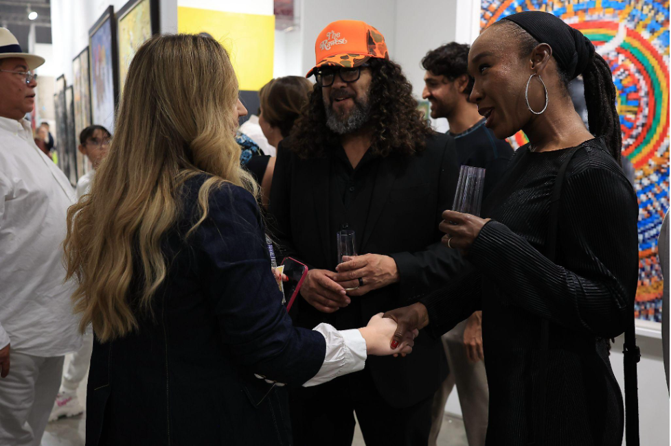 A candid moment at an art event where Venus Williams shakes hands with another woman, while two men stand nearby in a crowded gallery space.