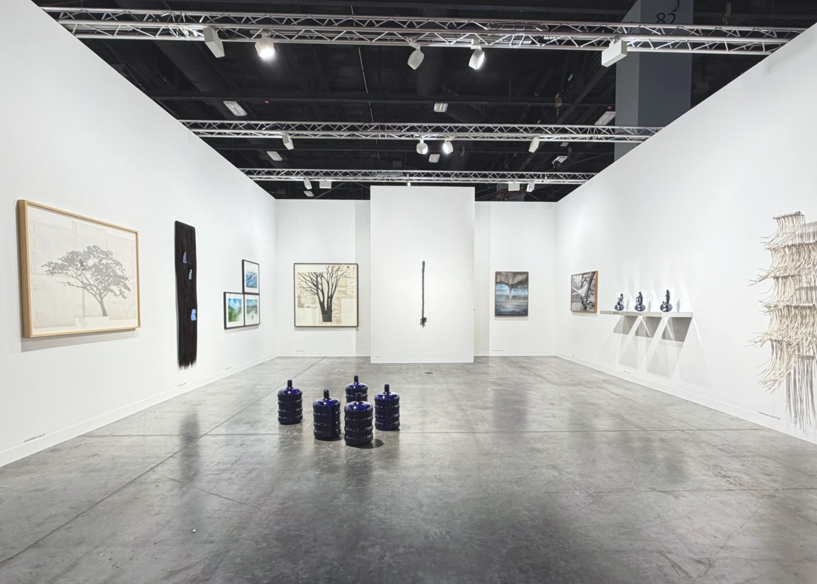 Minimal booth with framed landscape-style works on the walls and a cluster of dark blue ceramic vessels on the floor.