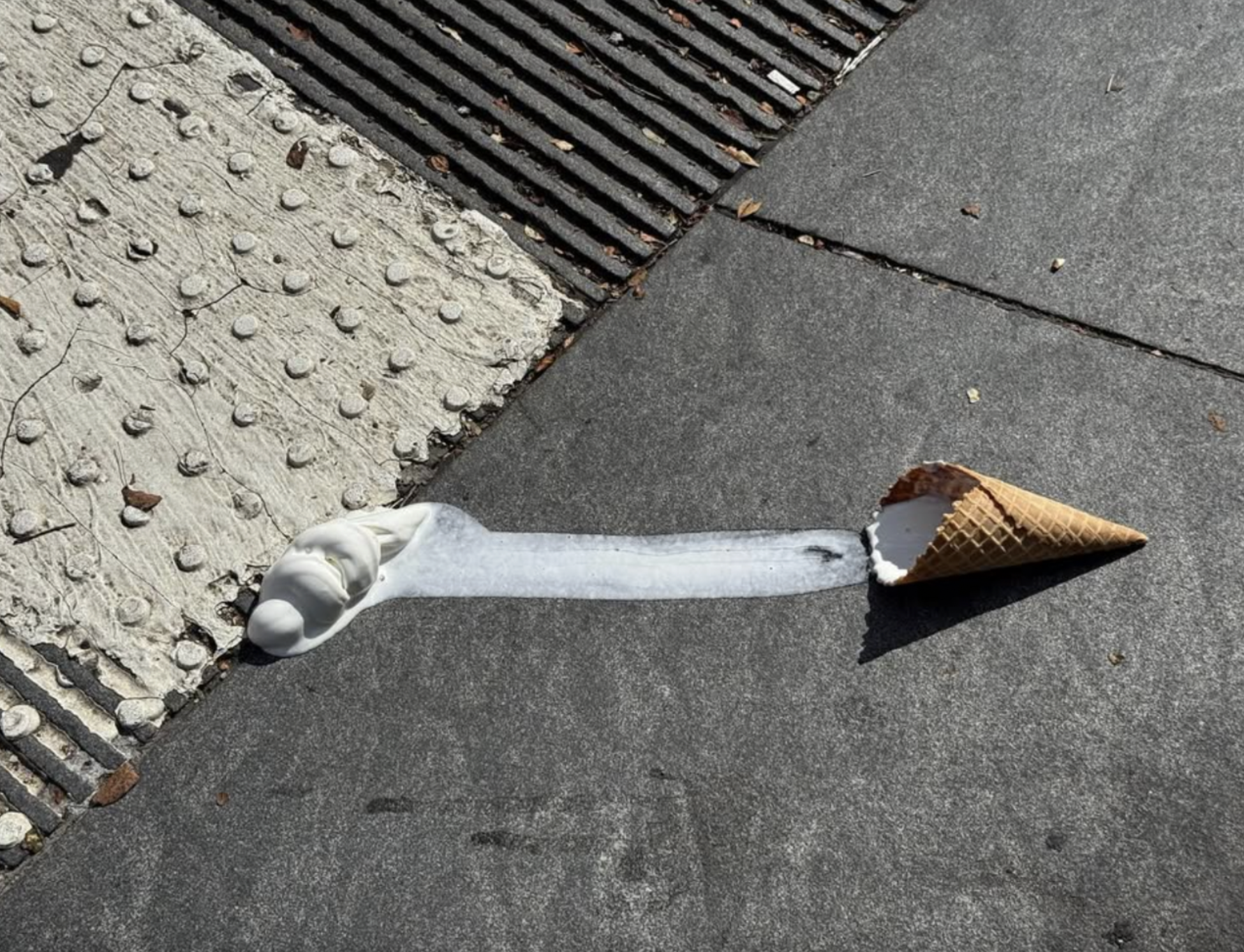Melted ice cream stretched across a sidewalk from cone to puddle.