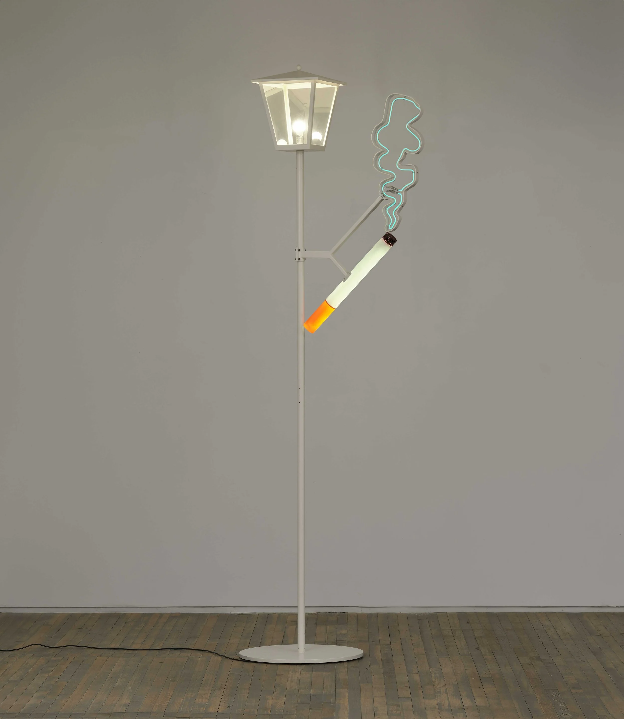 In a white gallery room, a thin, white lamplight stands with a neon cigarette sculpture attached by a branch of adjoining metal.