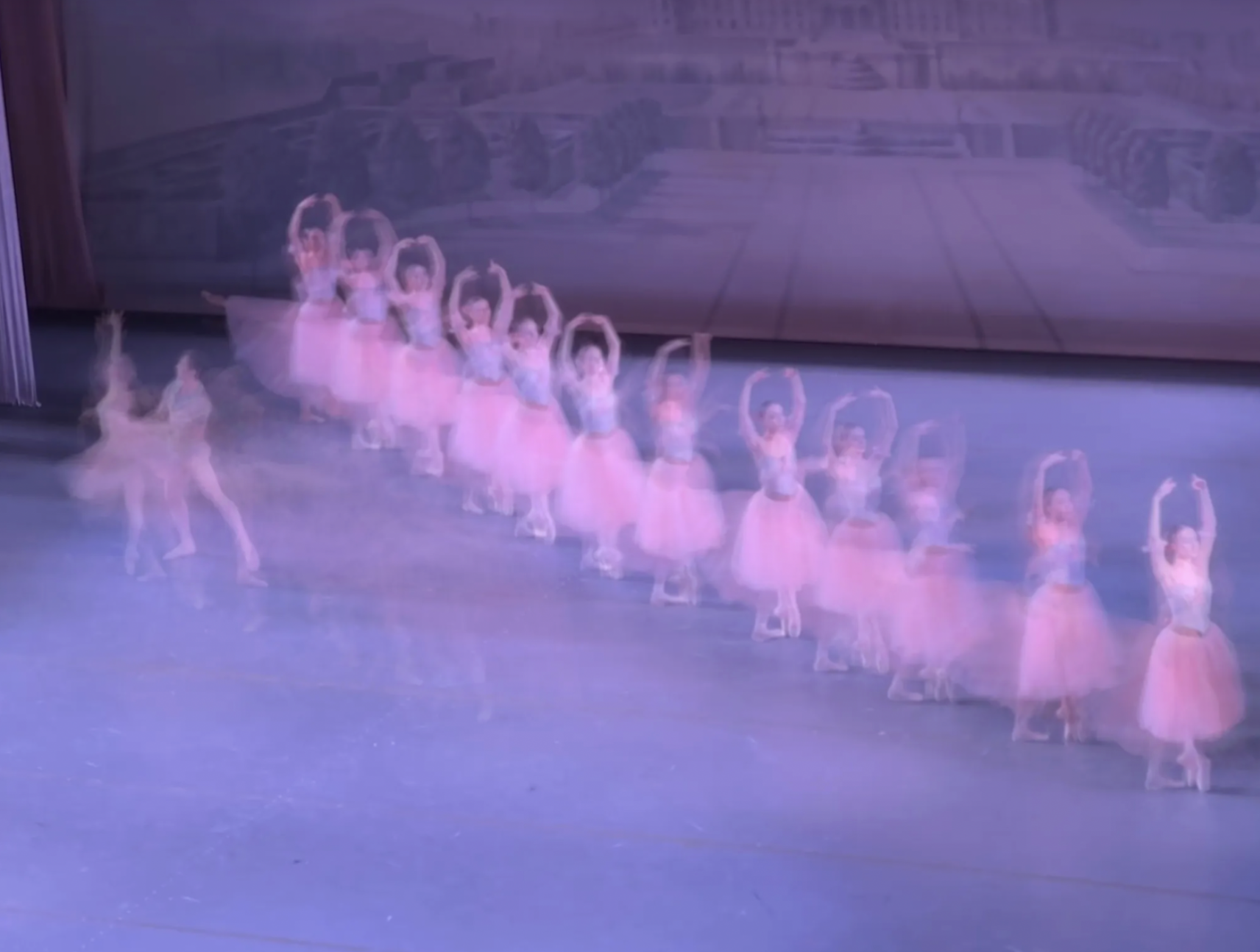 Motion-blurred line of ballet dancers in pink tutus performing on a stage.