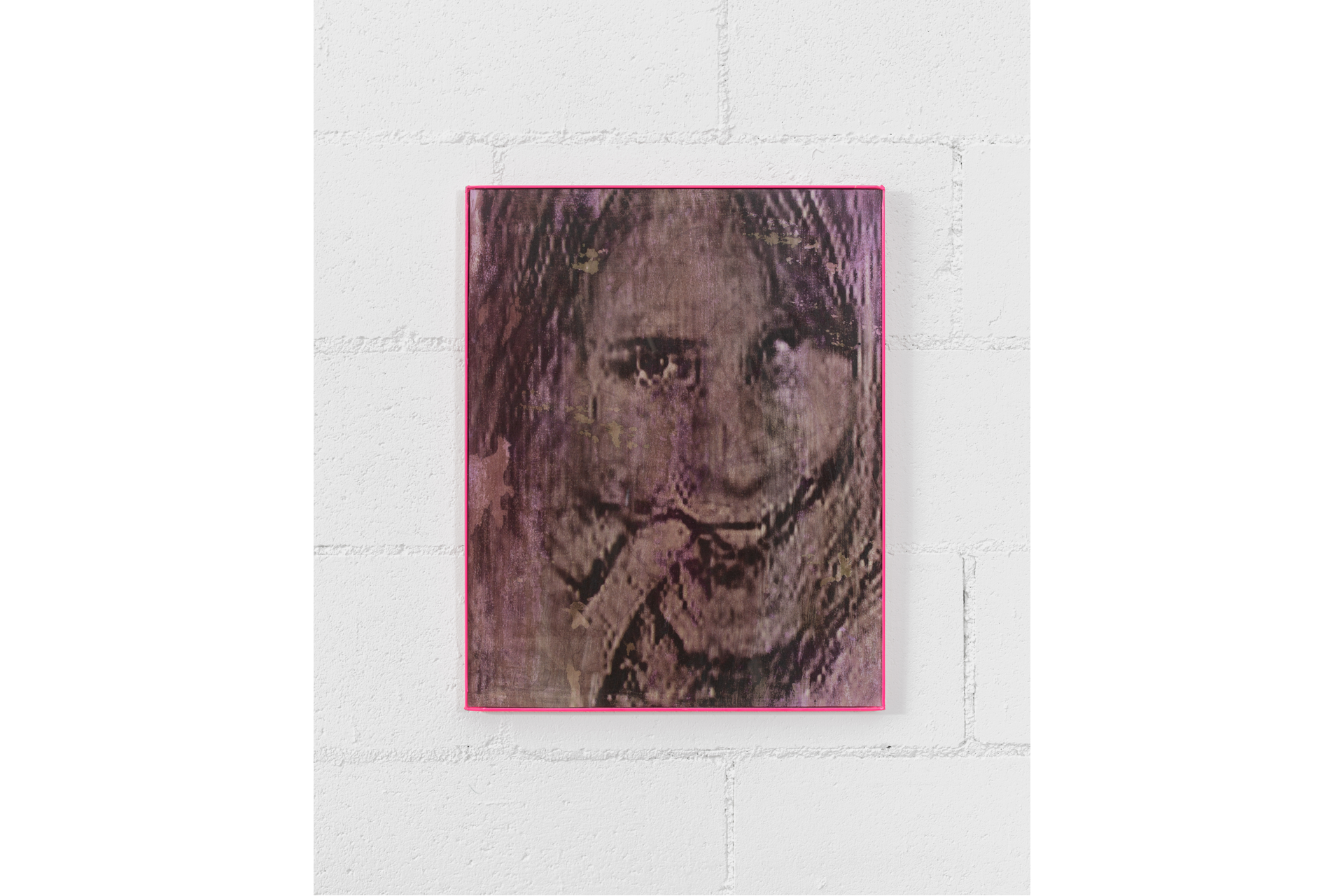 Mounted to a white wall, a thin pink framed 2-D work features a pixelated, smiling face, with eyes staring straight at the viewer.