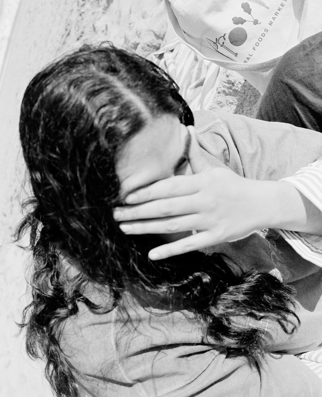 Black-and-white photograph of a person covering their face with one hand, hair falling forward.