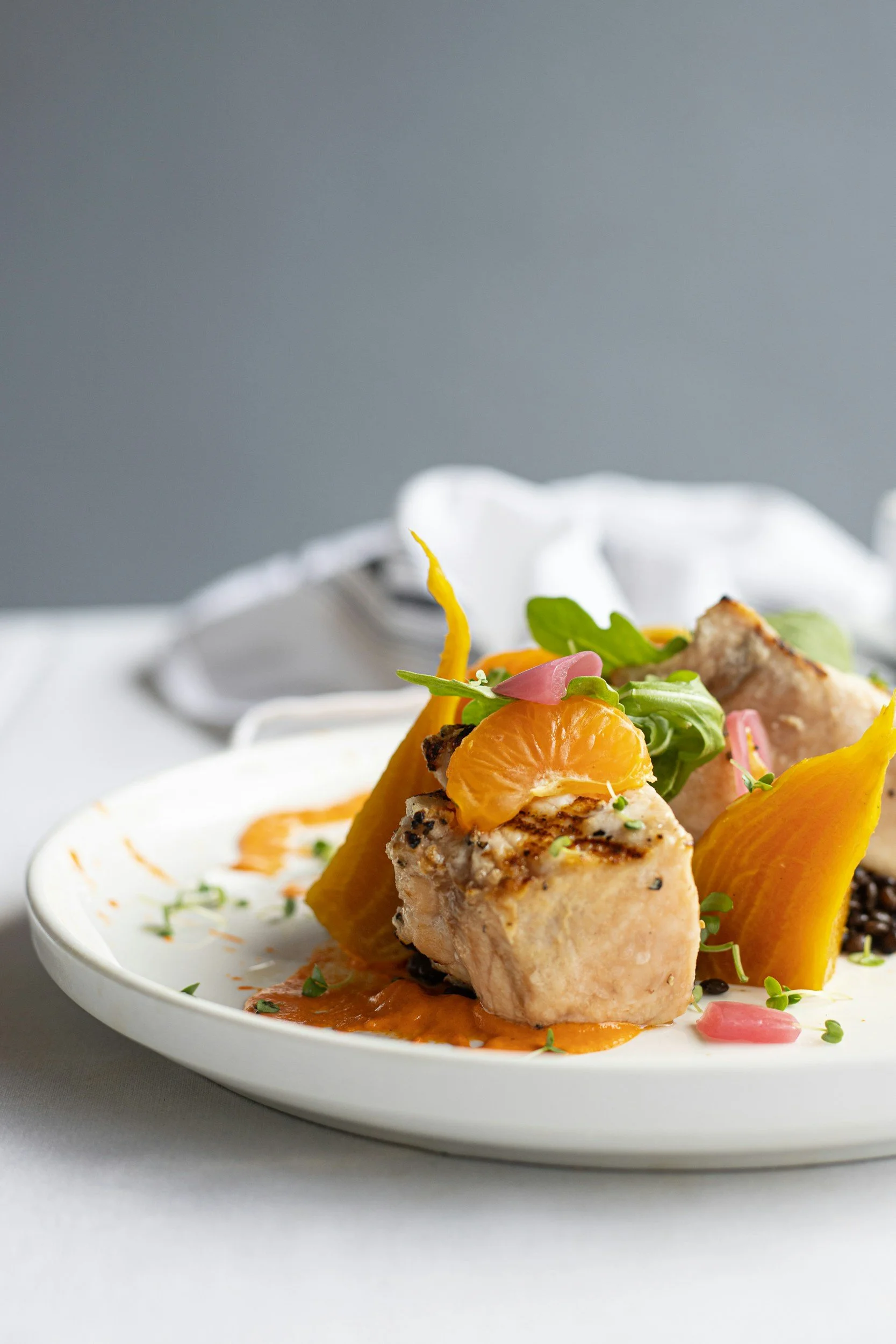 Close-up of a plated gourmet dish with cooked chicken, orange slices, greens, and sauce on a white plate to showcase a balanced meal encouraged by our Newcastle NSW and Hunter Valley NSW based dietitian to help build healthy nutrition habits.