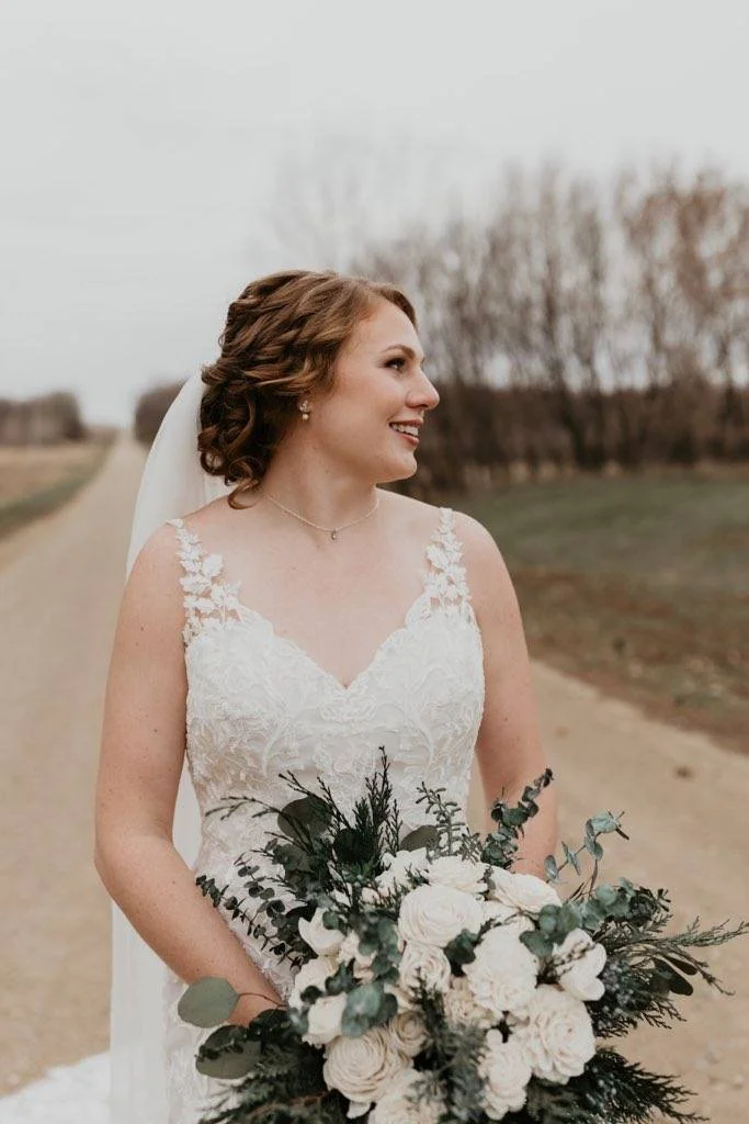 Bride in a wedding dress holding a bouquet of white flowers and greenery outdoors.