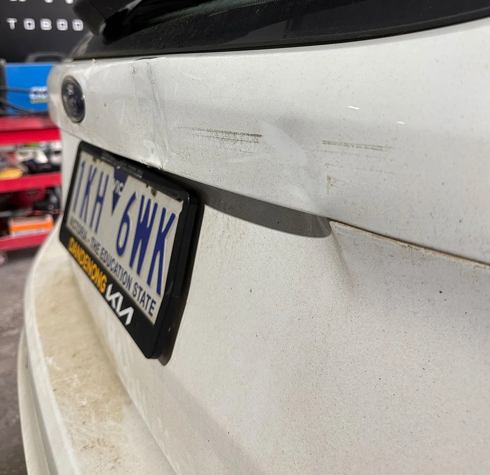 Scratch and dent damage on white hatchback car rear
