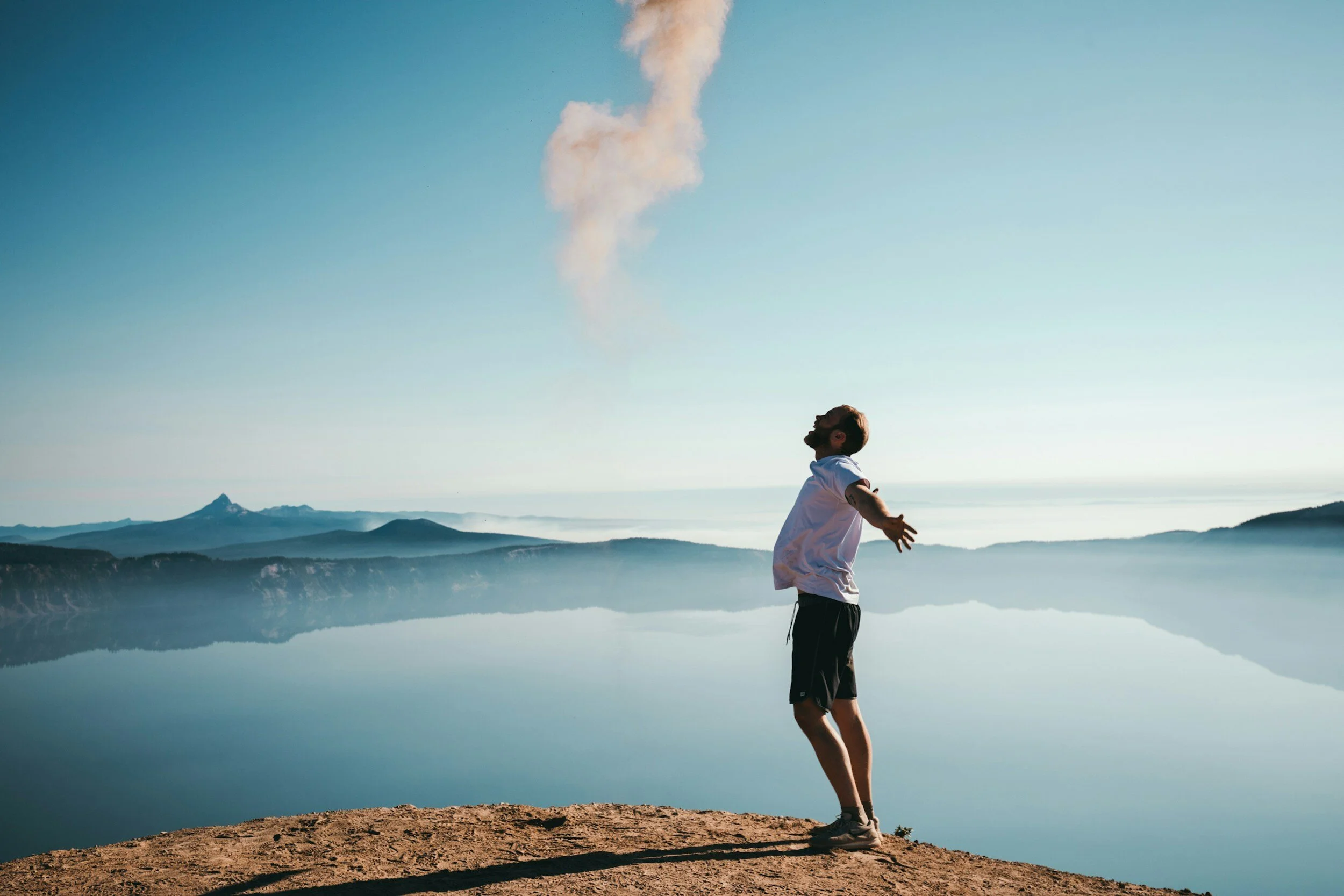En mann som feirer en livsforvandlende prestasjon, med åpne armer som slipper løs all den positive energien. I bakgrunnen skimtes det vakre havet og fjellene. Fotografi: Arkivfoto.