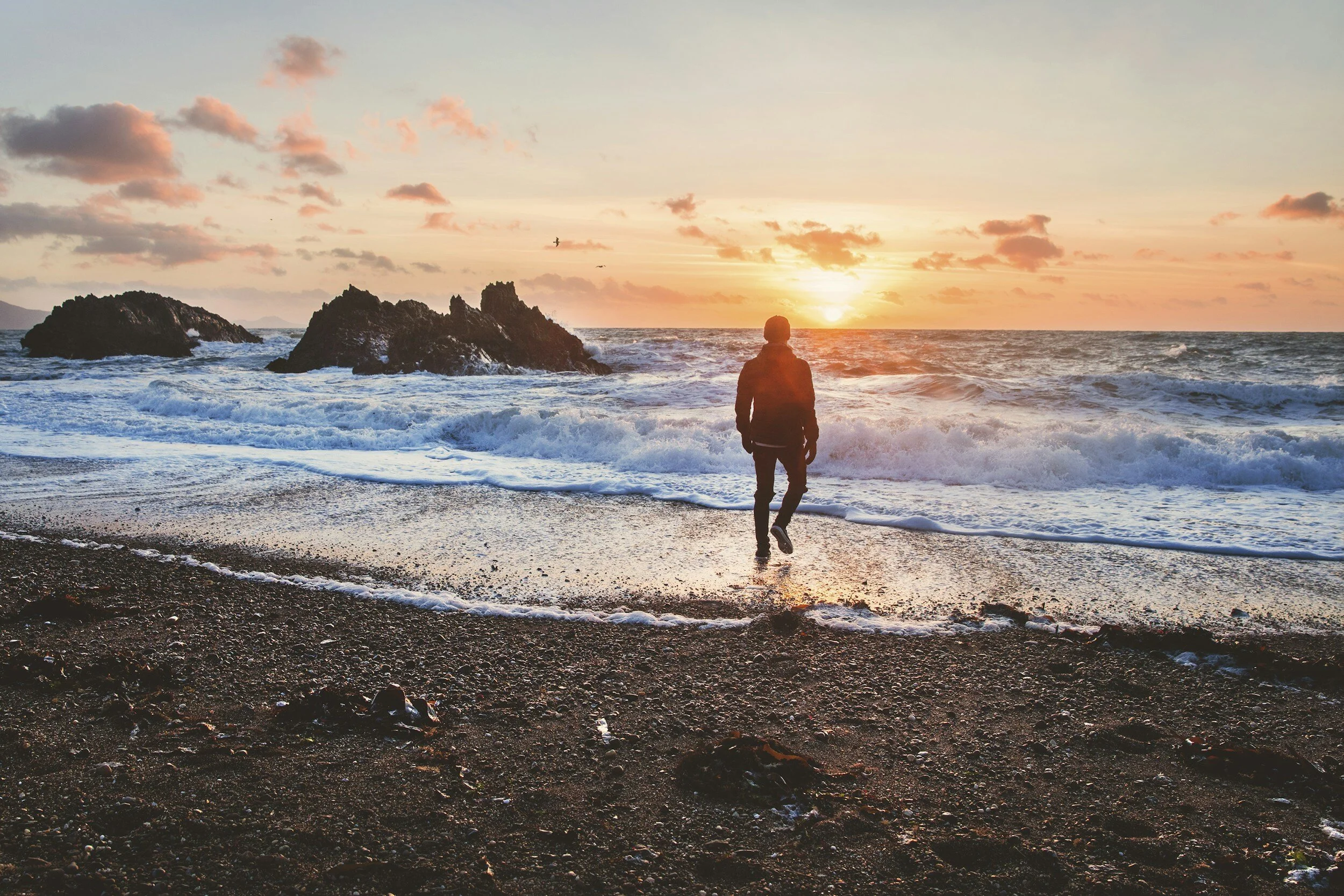 En mann går nedover en strand mot havet for å nyte en vakker solnedgang. Fotografi: Arkivfoto.