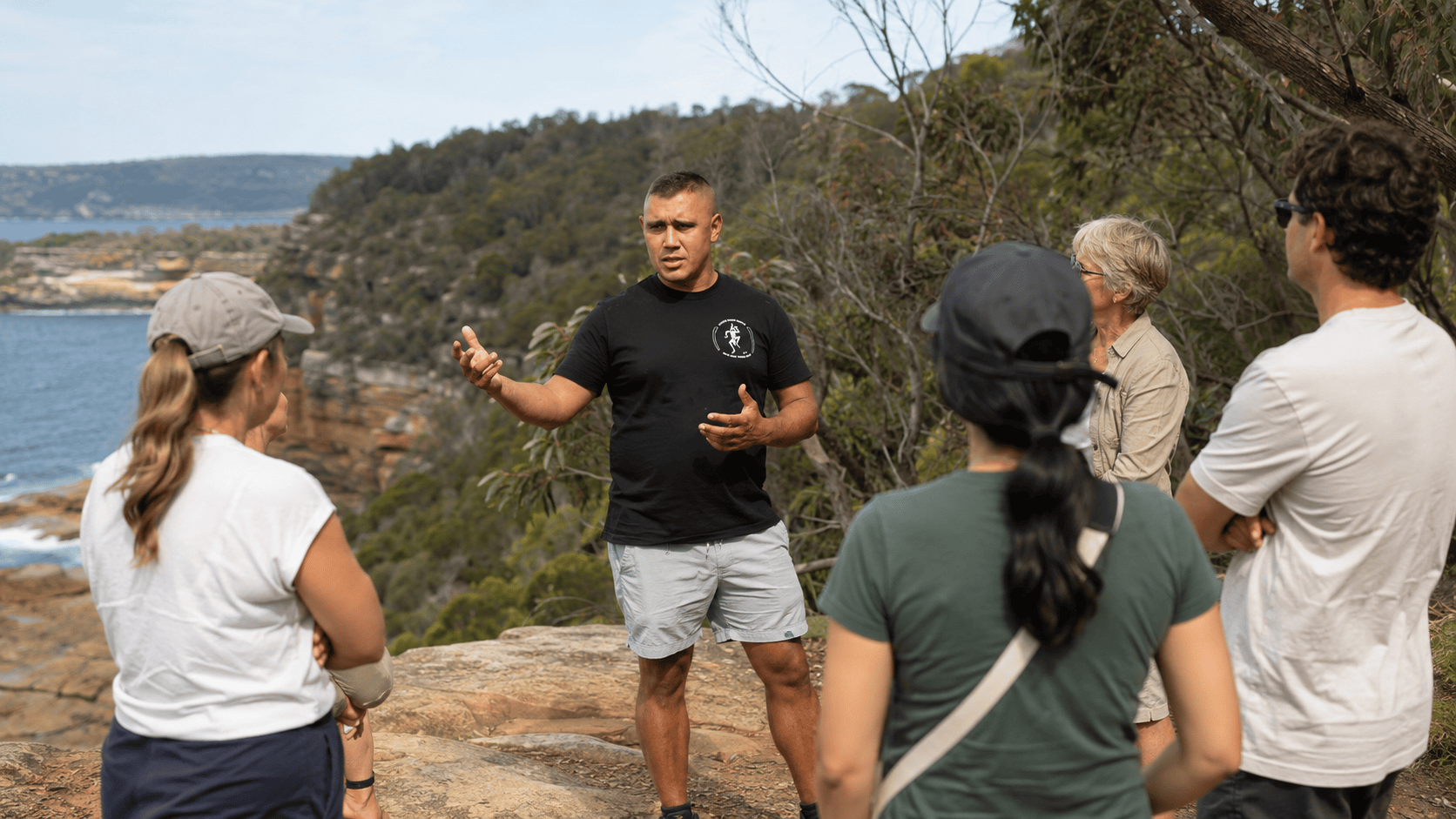 Aboriginal guide leading a coastal walking tour with guests in Sydney bushland.