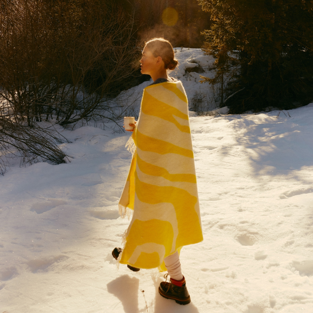 Woman standing outside in winter sunlight wrapped in a yellow blanket, symbolizing the role of natural light exposure in regulating mood and circadian rhythm.