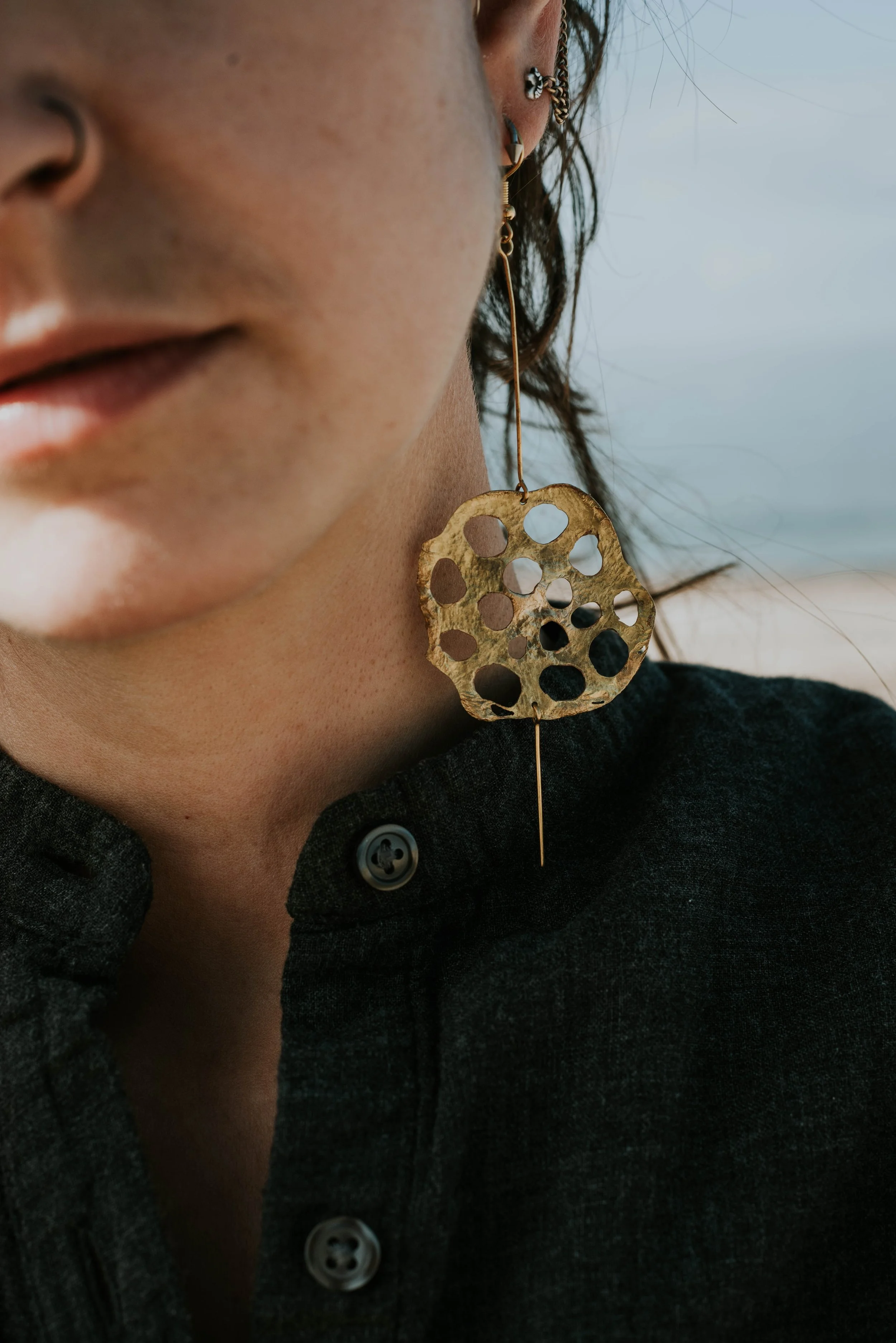 Close-up of handmade brass lotus seedpod earrings with organic texture and sculptural details
