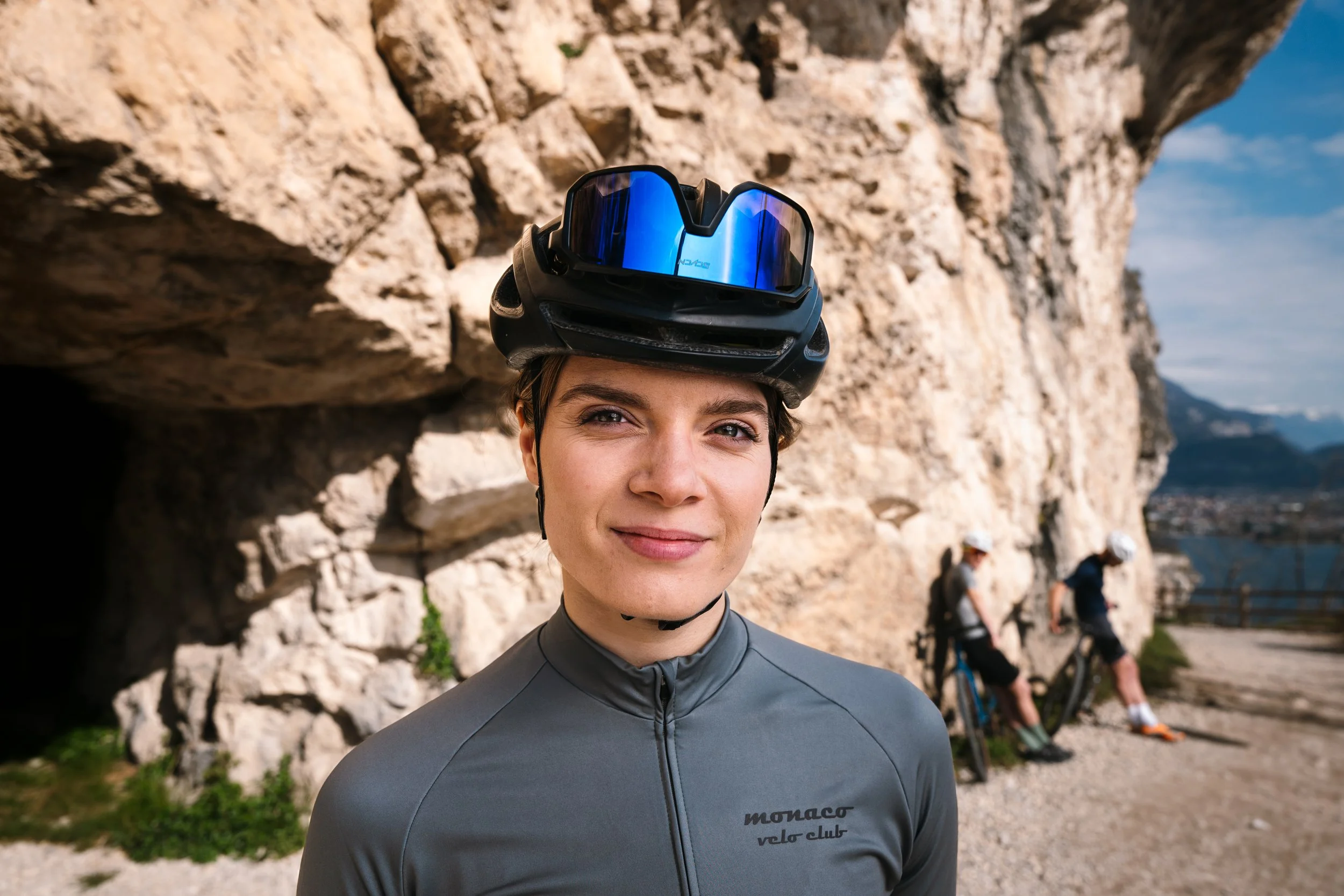 Frau mit Fahrradhelm und Brille vor Felsformation, im Hintergrund zwei Personen mit Fahrrädern. Hotelfotografie, Hotelvideografie, Tourismus, Videoproduktion für Tourismus