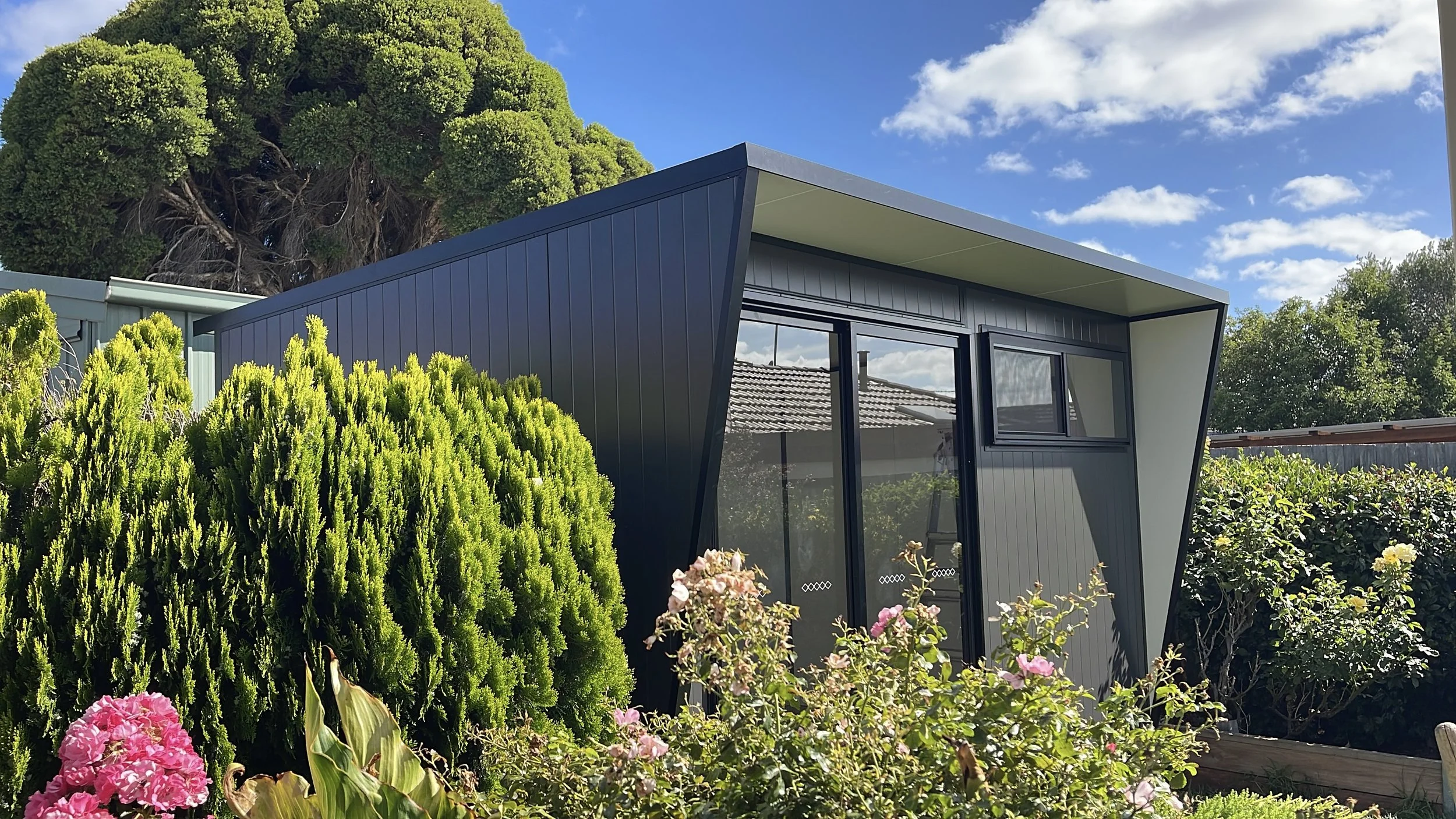 Modern backyard pod in Monument colour with VJ groove cladding, cantilever roof design, and large sliding glass door, installed in a landscaped Melbourne garden.