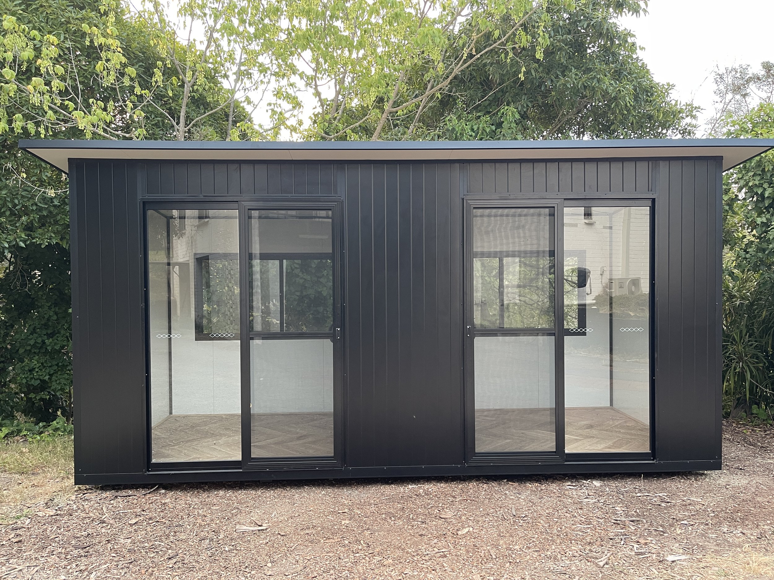 Lifestyle Backyard Pods black Colorbond pod featuring VJ groove exterior cladding and sliding glass doors, custom built and installed on site.