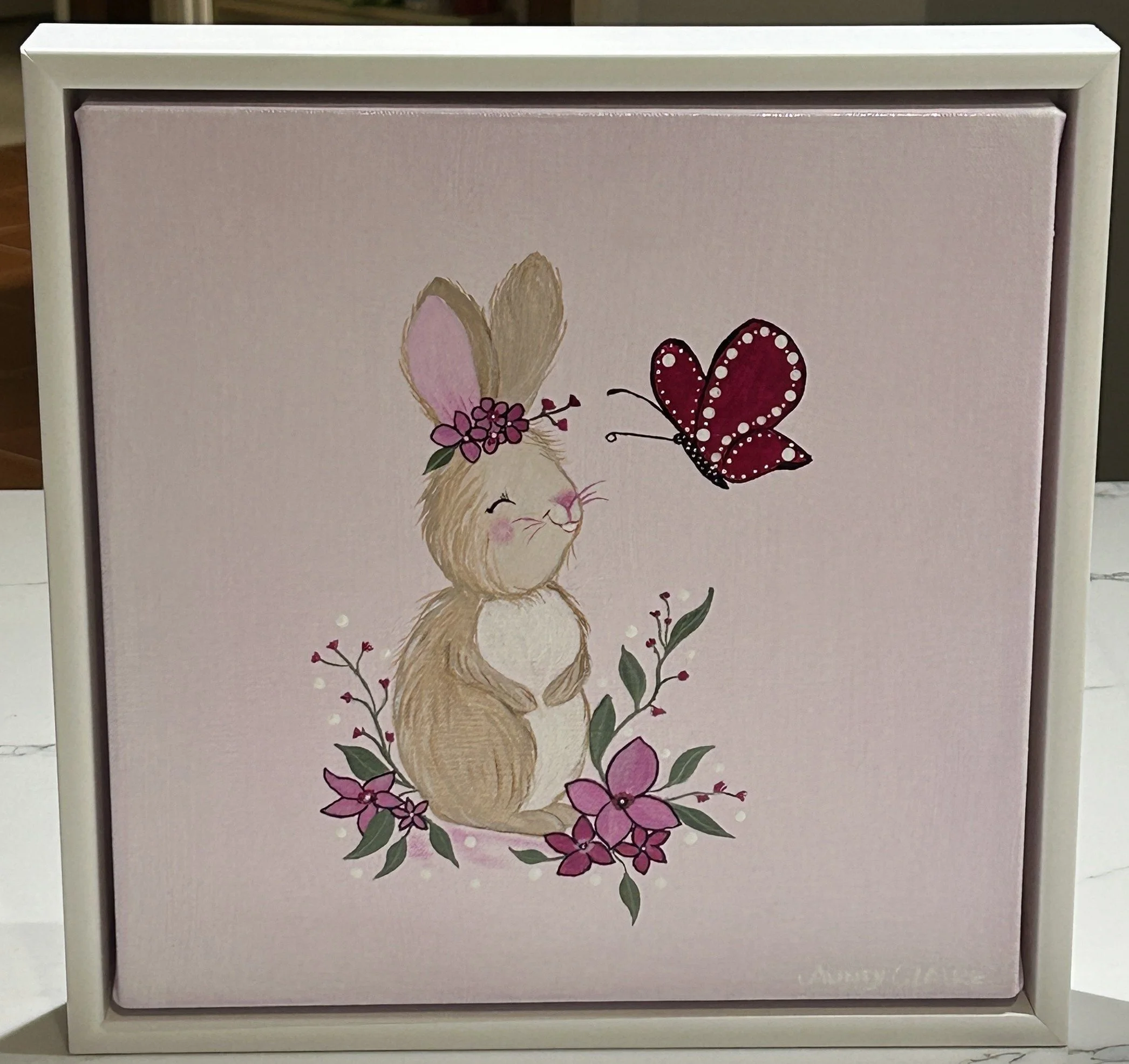 Decorative box frame featuring a beige rabbit with pink ears, surrounded by pink flowers and green leaves, and a red butterfly with white dotted patterns.