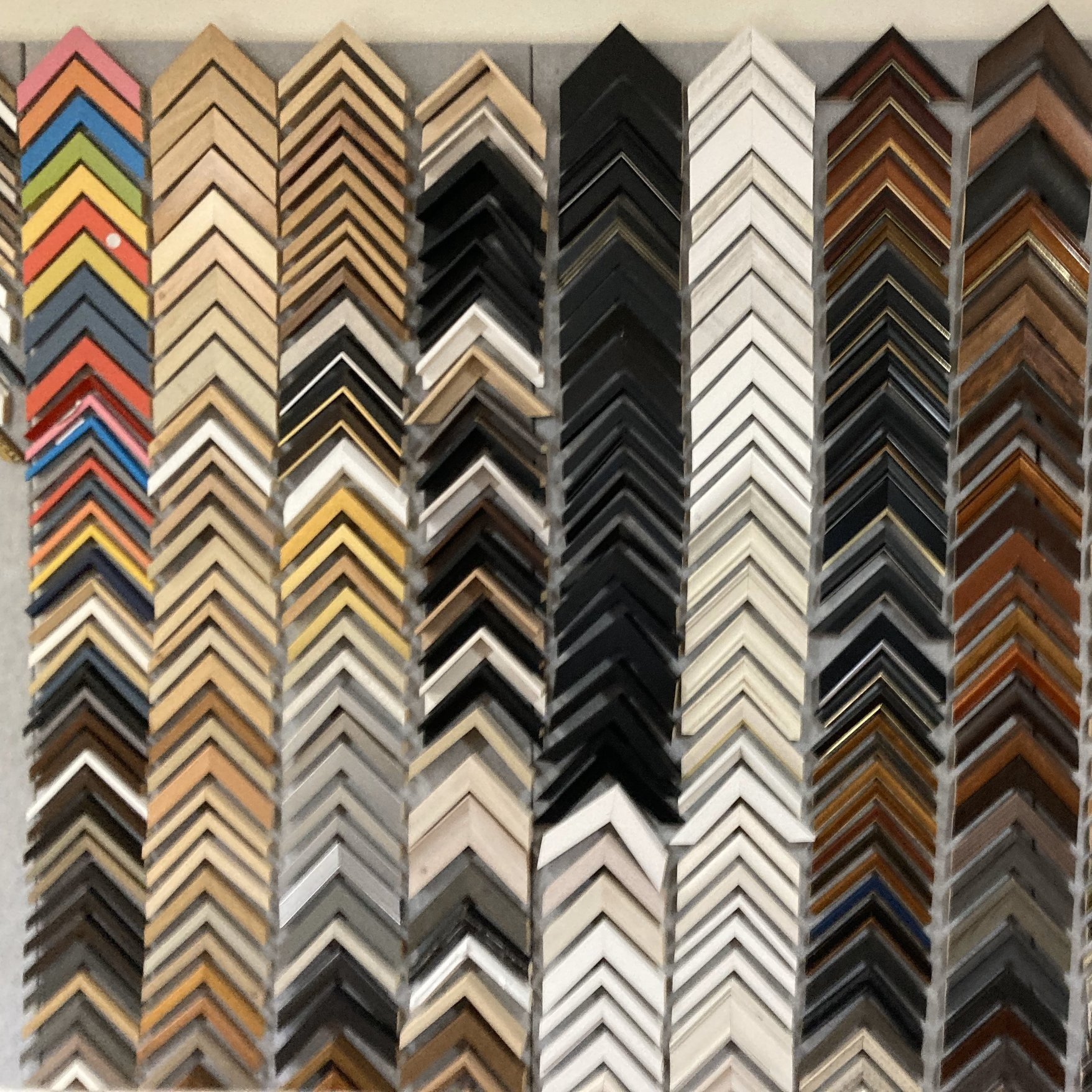 Display of various picture frame corner samples in multiple colours and finishes, organised in vertical rows.