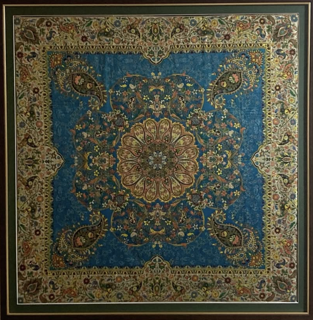 A detailed, colorful Persian-style carpet with a floral and paisley pattern, featuring a central medallion on a blue background surrounded by intricate borders with floral motifs.