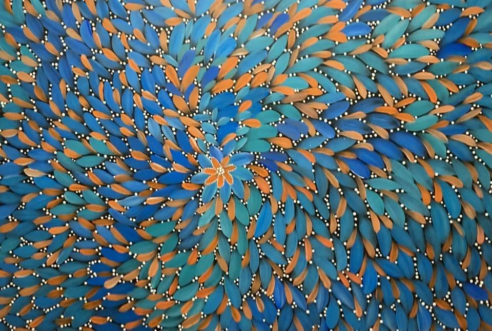 A vibrant, colorful aboriginal dot painting with swirling patterns of blue and orange teardrop shapes, and a floral design in the center.
