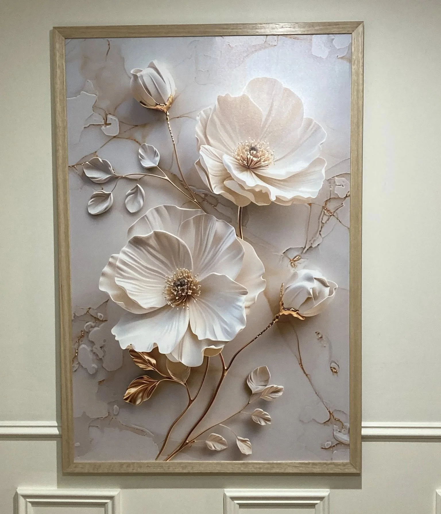 Decorative artwork of white 3D flowers with gold accents on a marble background, framed with a light wood frame.