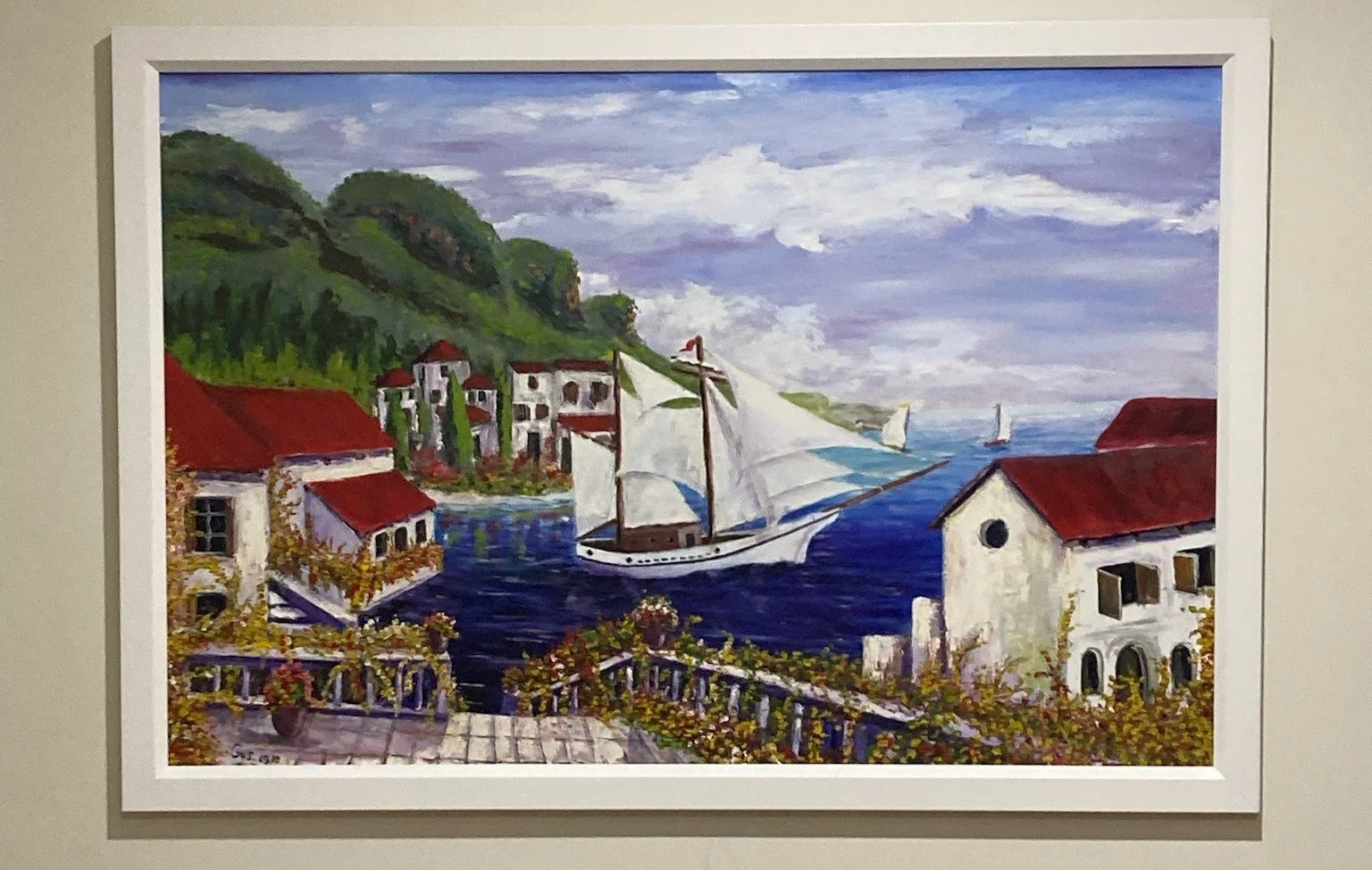 Painting of a coastal village with white houses, red roofs, and a sailboat on the water, surrounded by green hills and a cloudy sky.