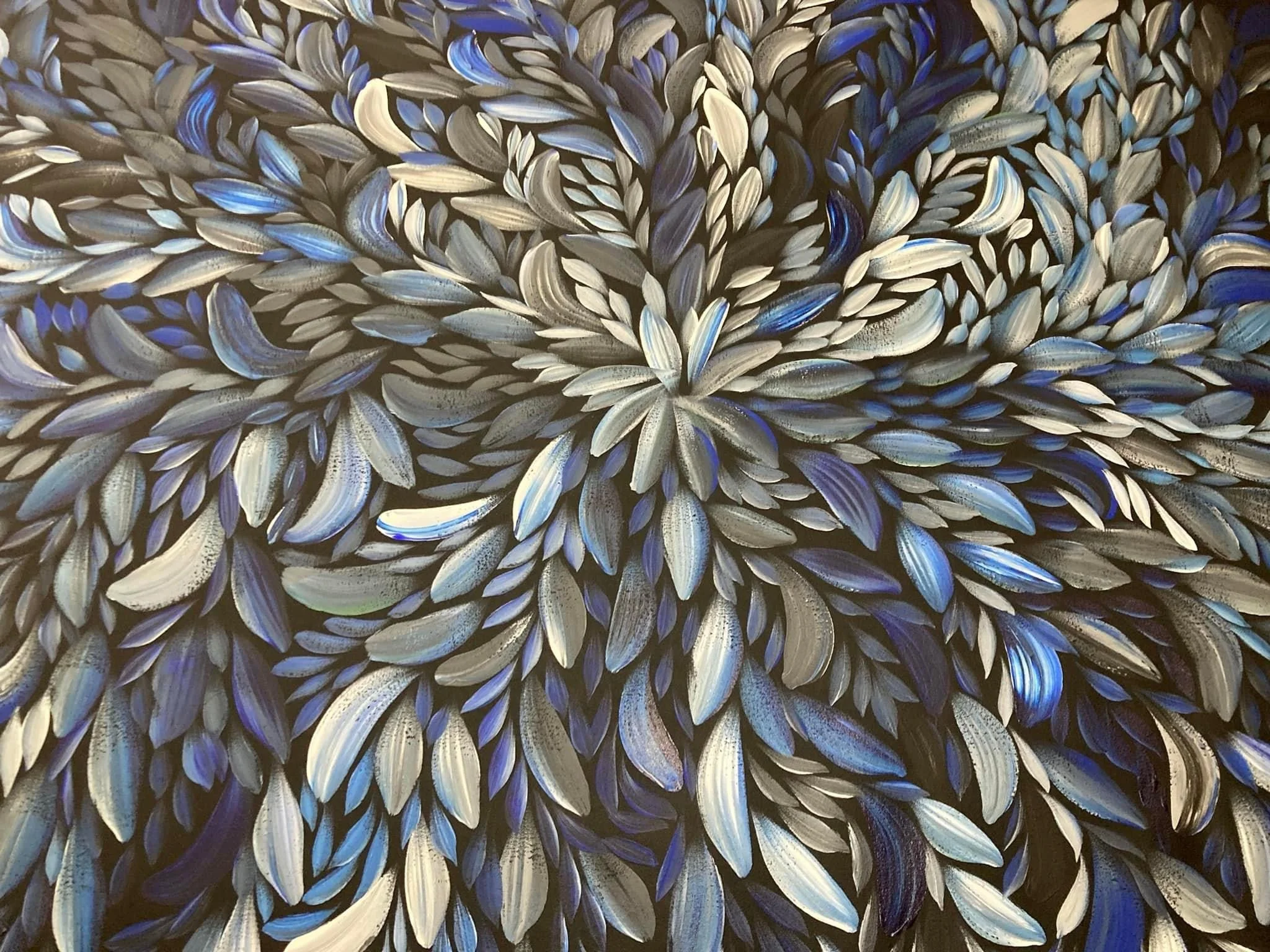 Close-up view of a textured wall painting featuring numerous layered, elongated brushstrokes in shades of black, blue, and gray, arranged in a swirling pattern.
