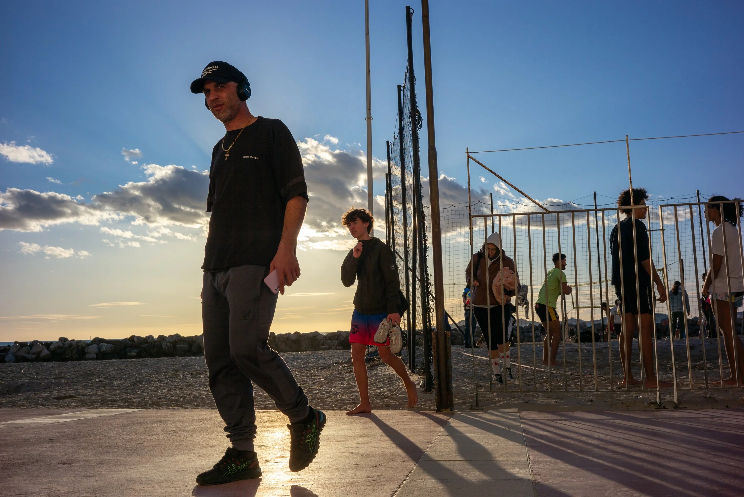 Groupe de jeunes personnes jouant au beach-volley sur la plage avec un ciel nuageux au coucher du soleil.
