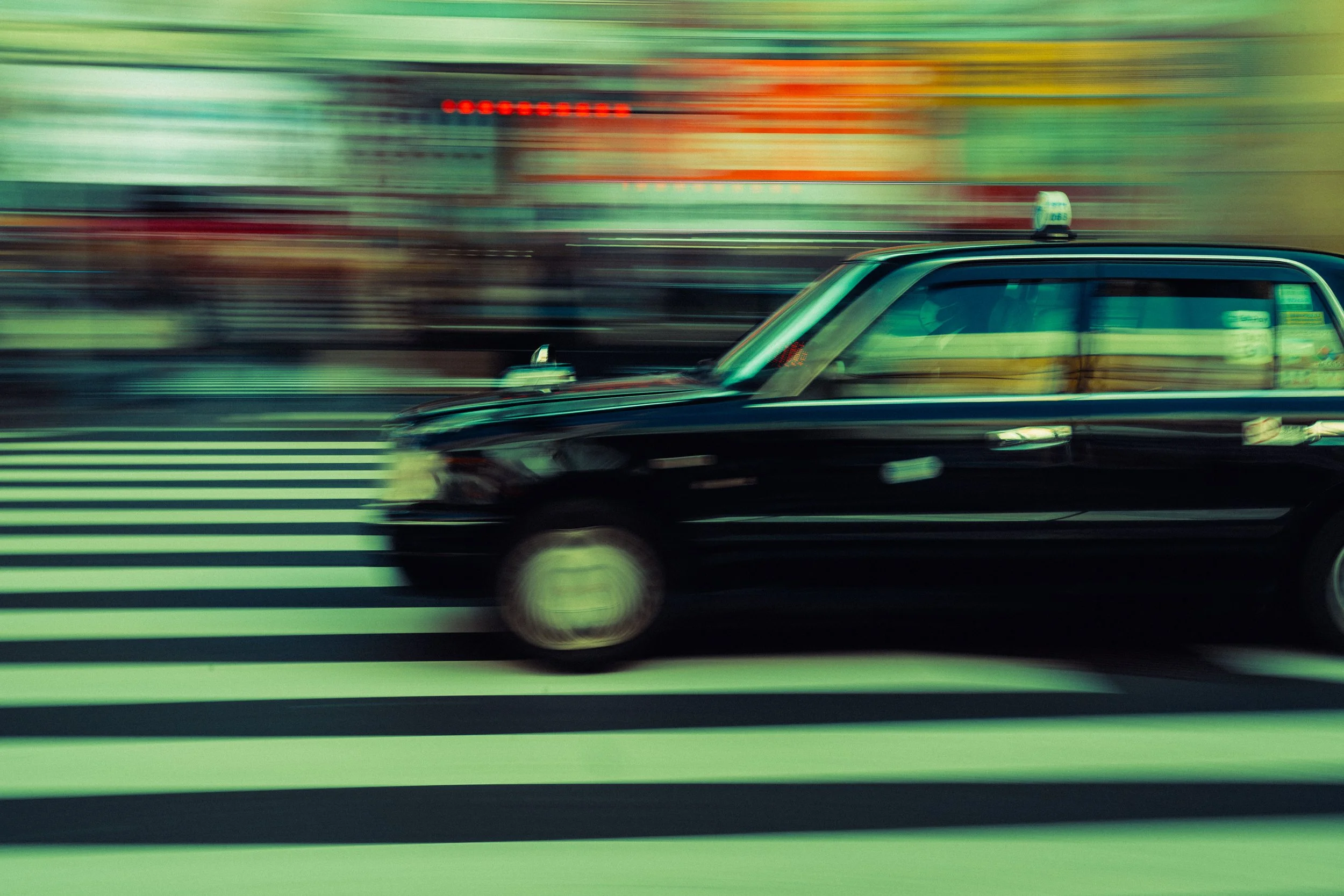 Une voiture noire à taxi traverse un passage piéton dans une ville en mouvement, avec un arrière-plan flou.