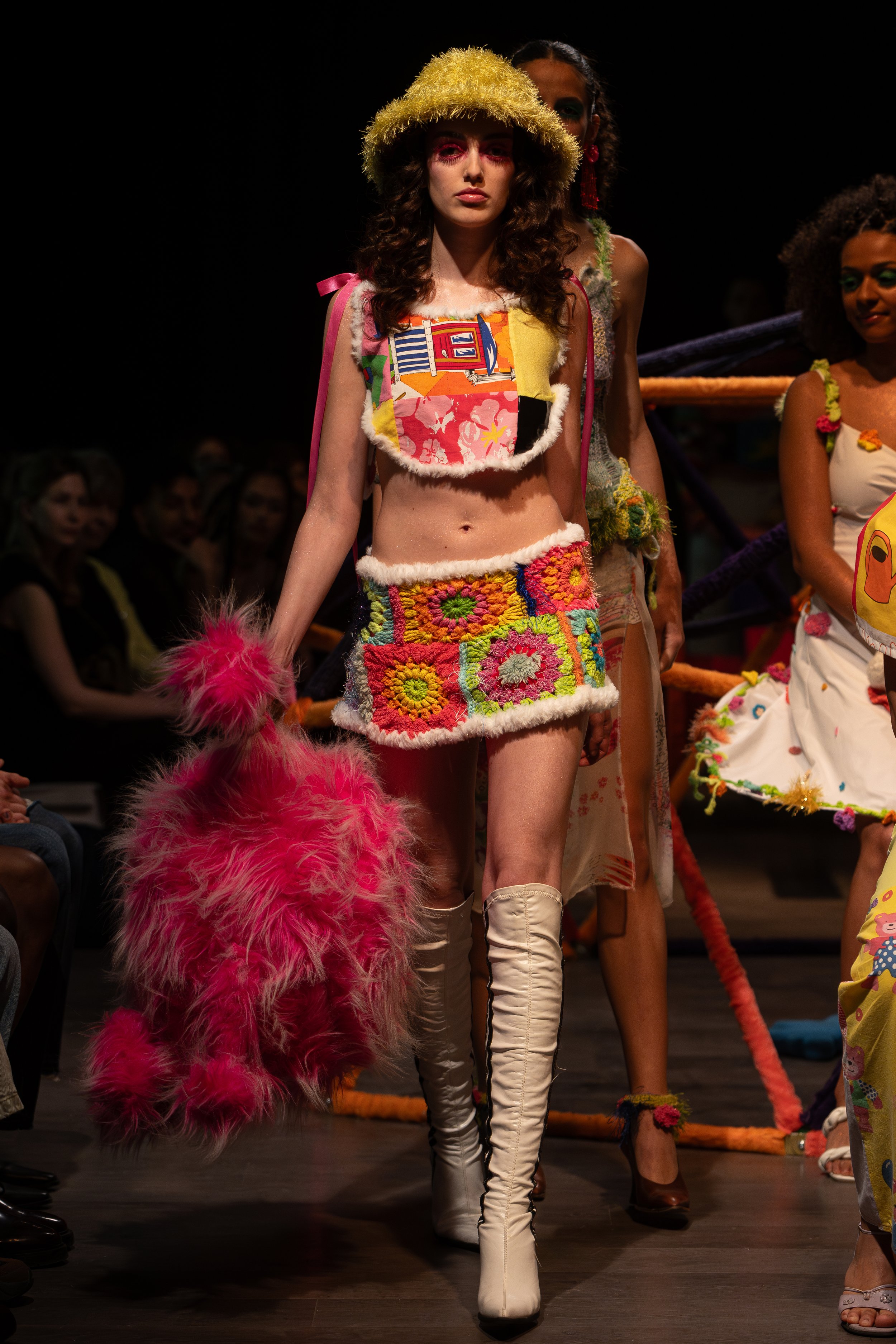 Fashion models walk down the runway in colorful, textured clothing with fluffy accessories, during a fashion show.
