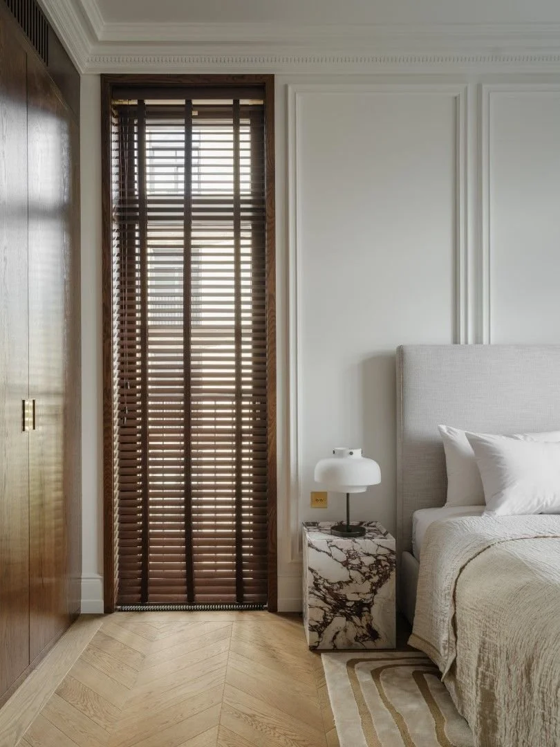 Cozy bedroom with wooden blinds, marble side table, and soft neutral tones.