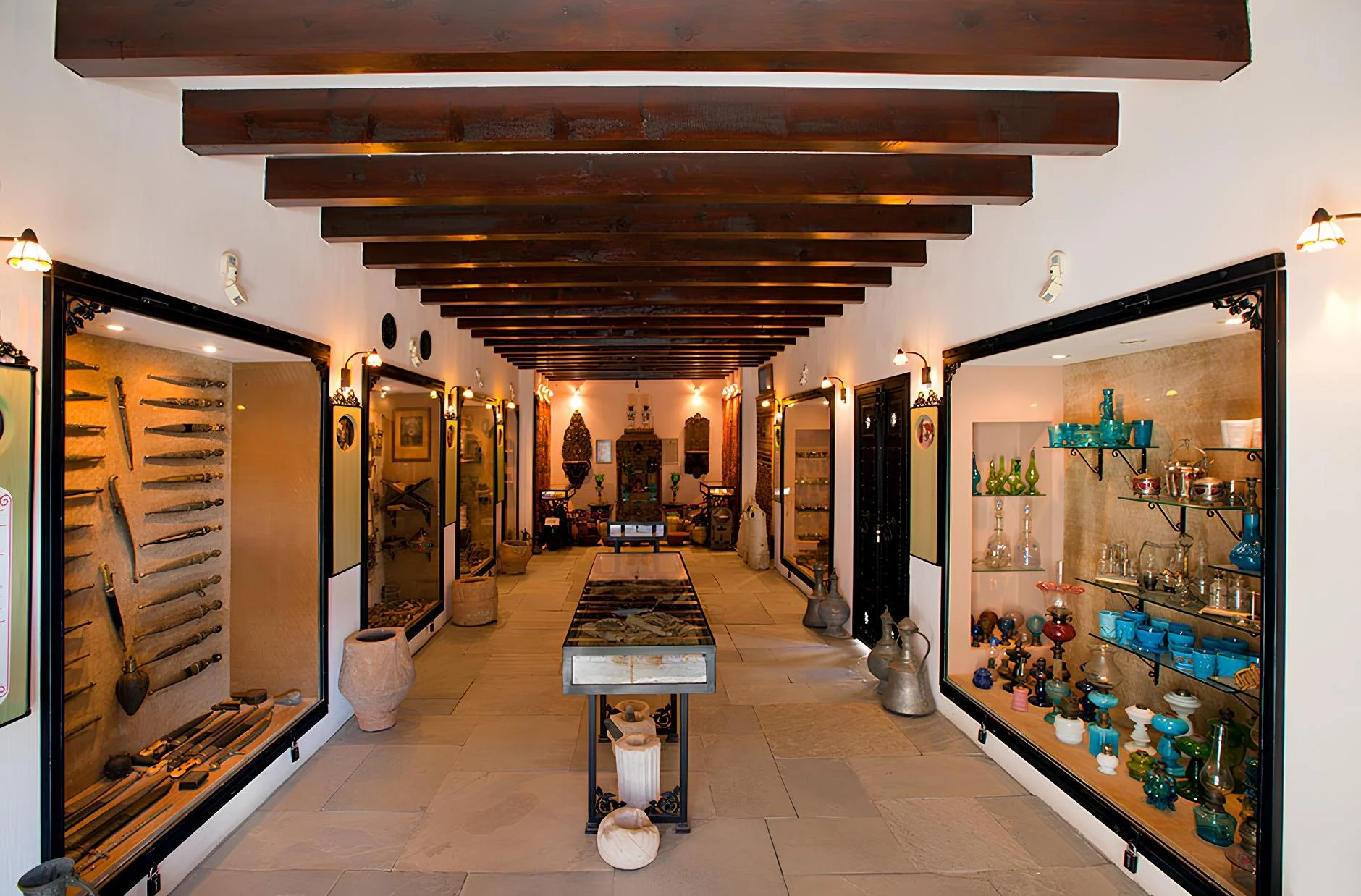 Interior of a museum or gallery with display cases of artifacts and collectibles, wooden beams on the ceiling, and decorative lighting.