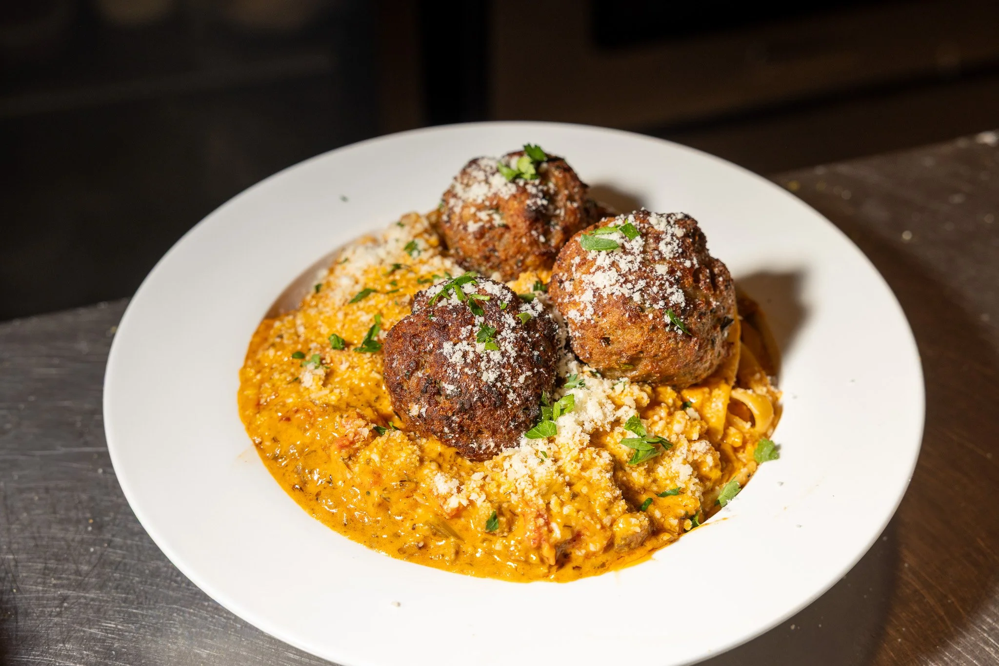 A plate of ragu with tomato sauce, topped with three meatballs, garnished with grated cheese and chopped parsley.