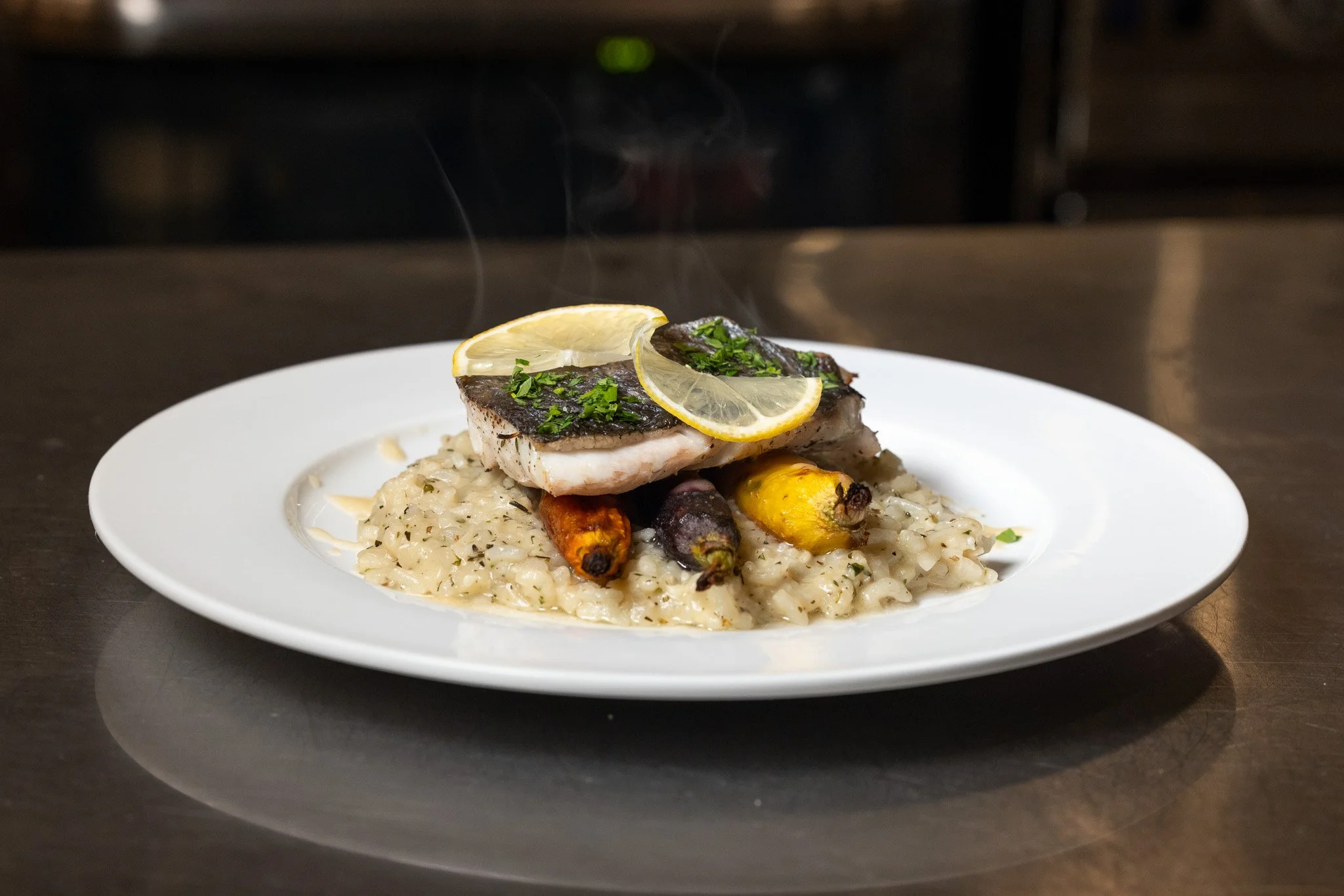 A plate of Fish Del Giorno, containing a lemon herb risotto, carrot, burro bianco