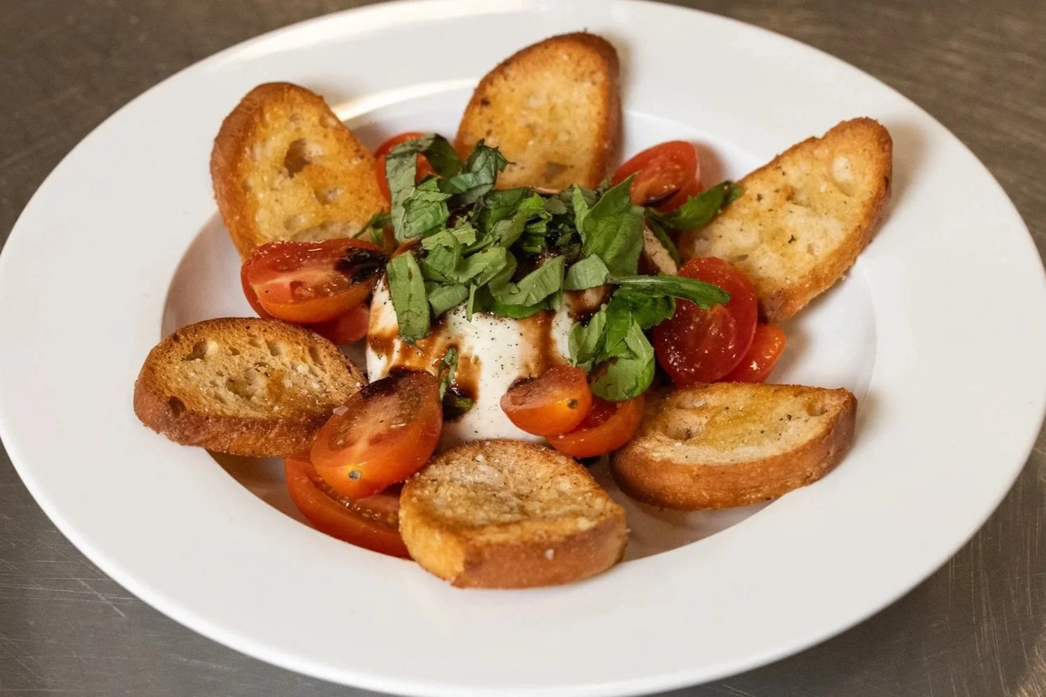 Plate of burrata with fresh mozzarella, tomato, basil, balsamic fig glaze, and crostini.