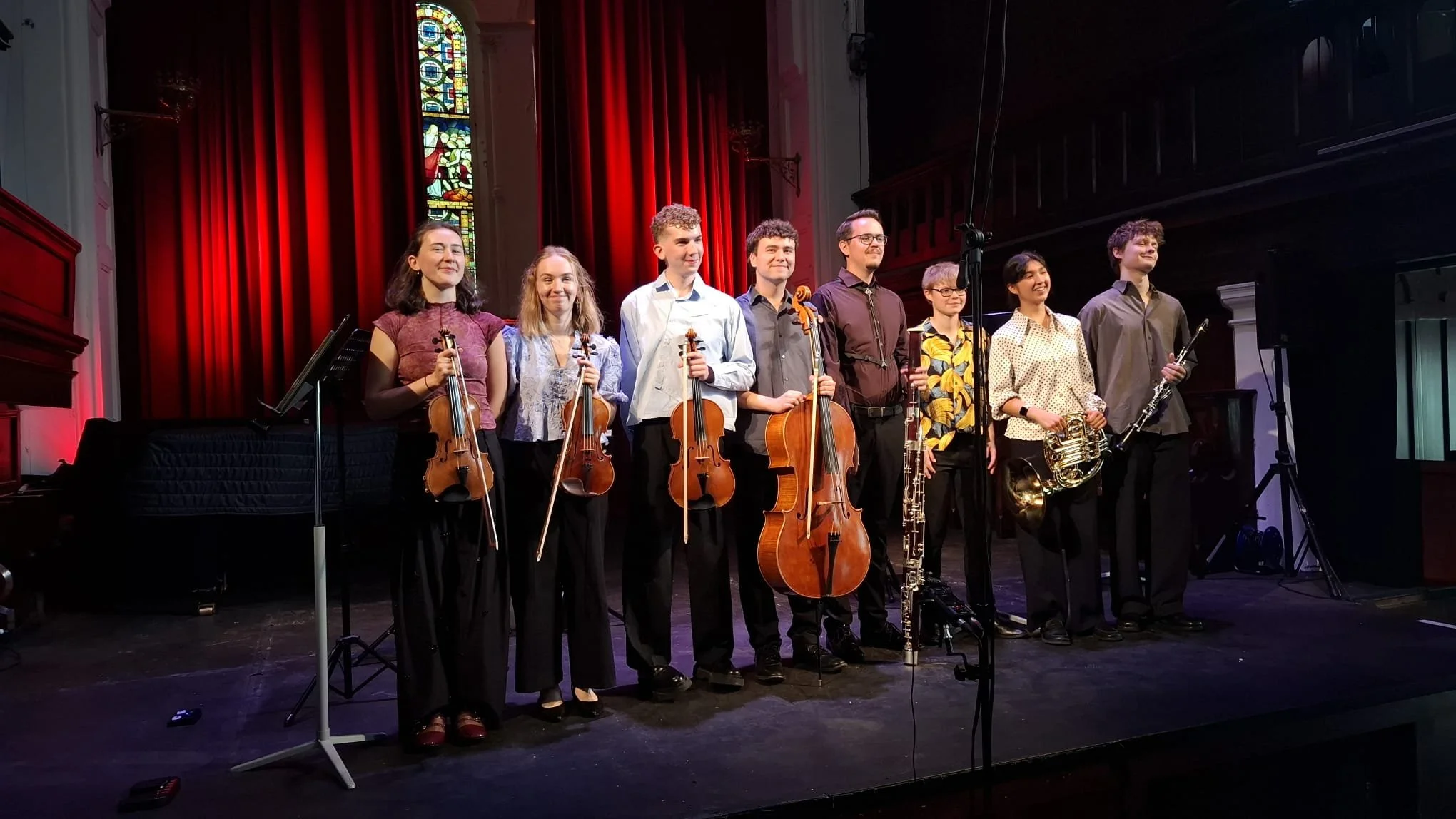 A group of nine young musicians standing on stage holding various musical instruments at Triskel Arts Centre Cork.