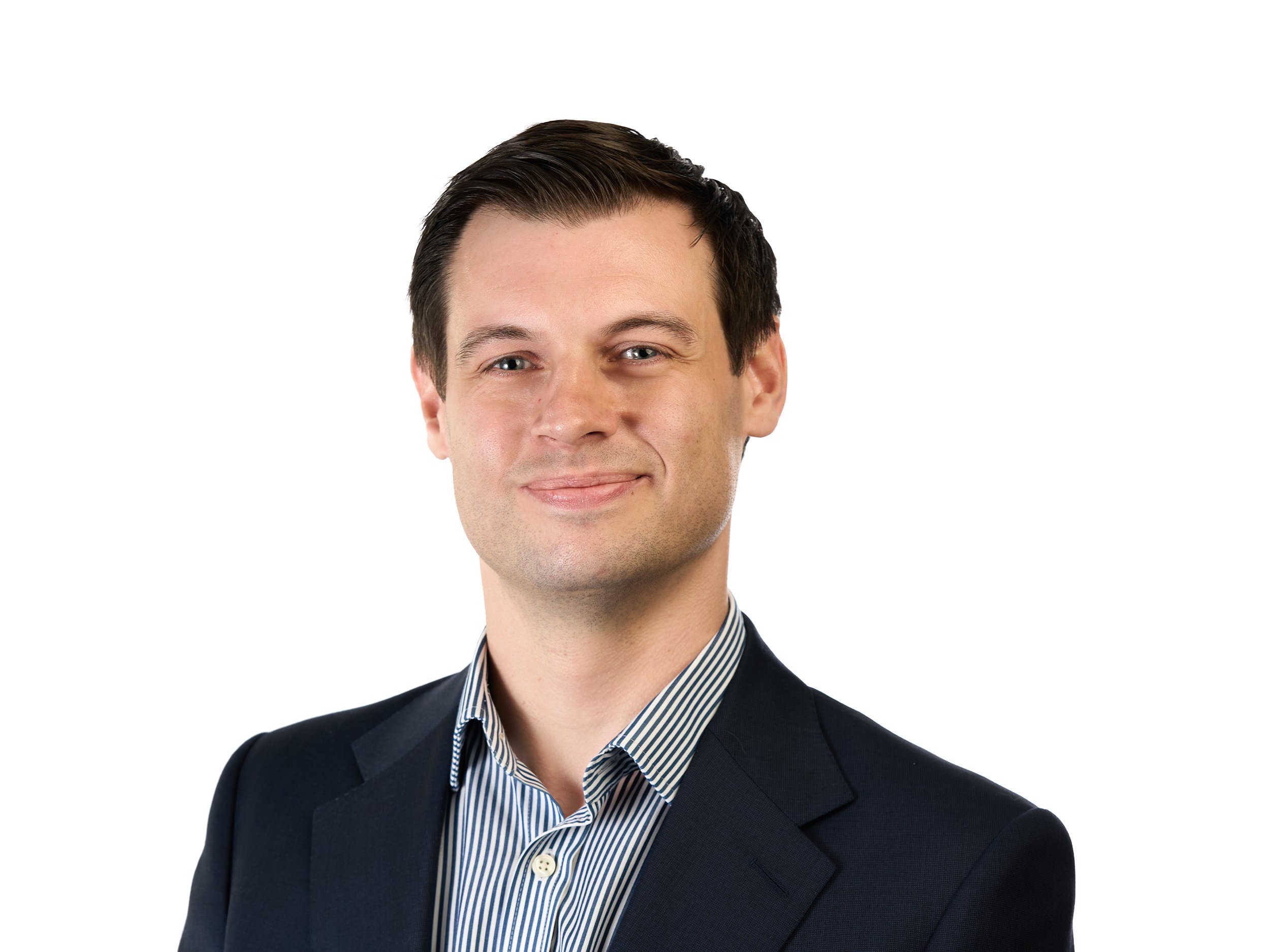 A professional headshot of a young man in a white shirt and dark blazer, smiling, with a plain white background.