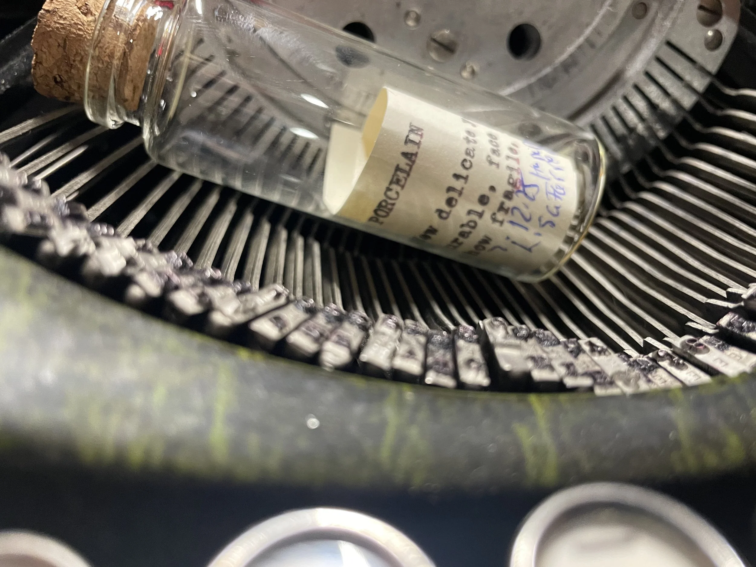 A glass bottle lying on its side in a machine with metal rollers, labeled with handwritten notes.