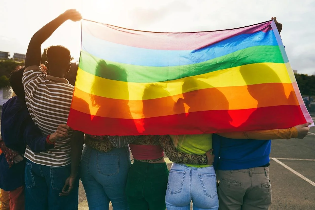 Group of people holding a rainbow pride flag outdoors during sunset.