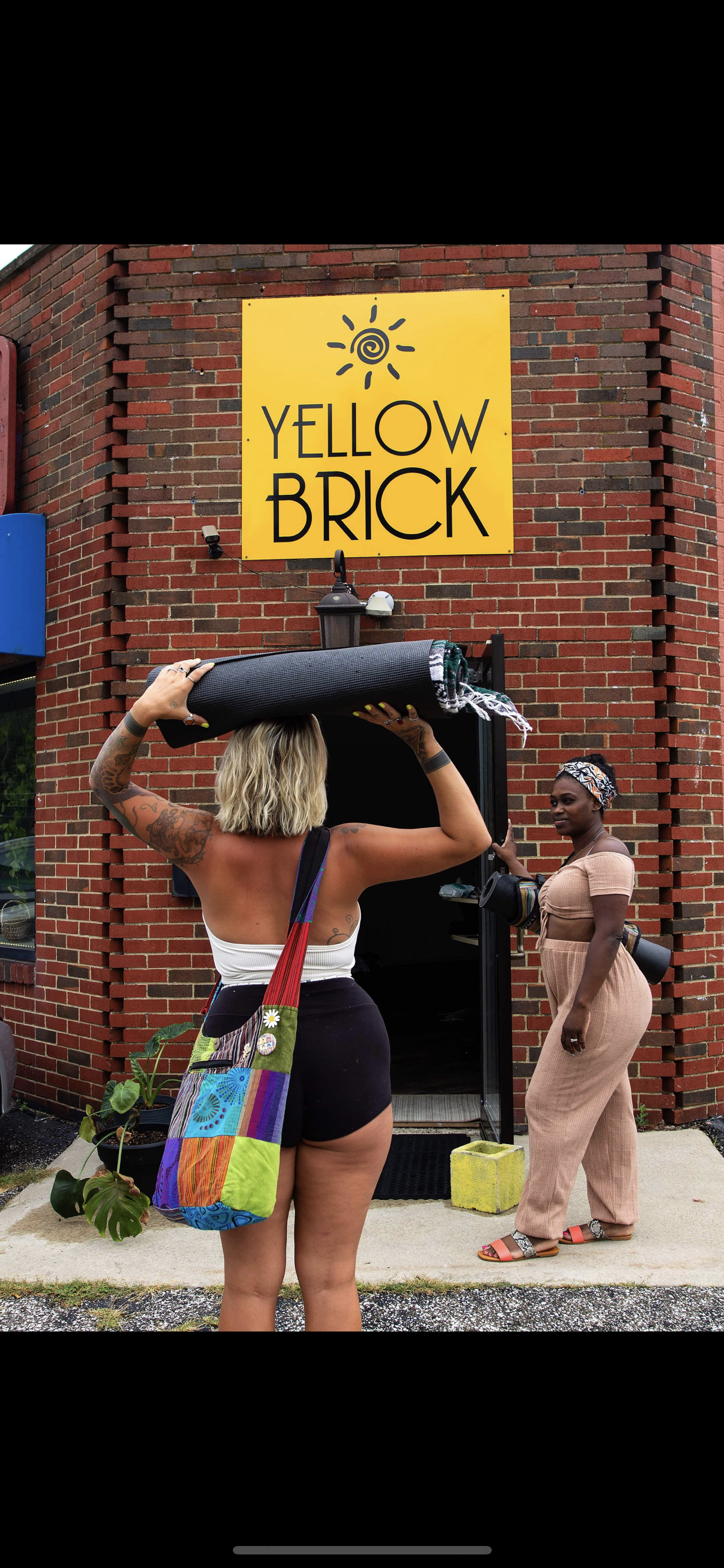 Two women practicing meditation with eyes closed, sitting cross-legged on mats, hands on their chests and stomachs, in a well-lit room.