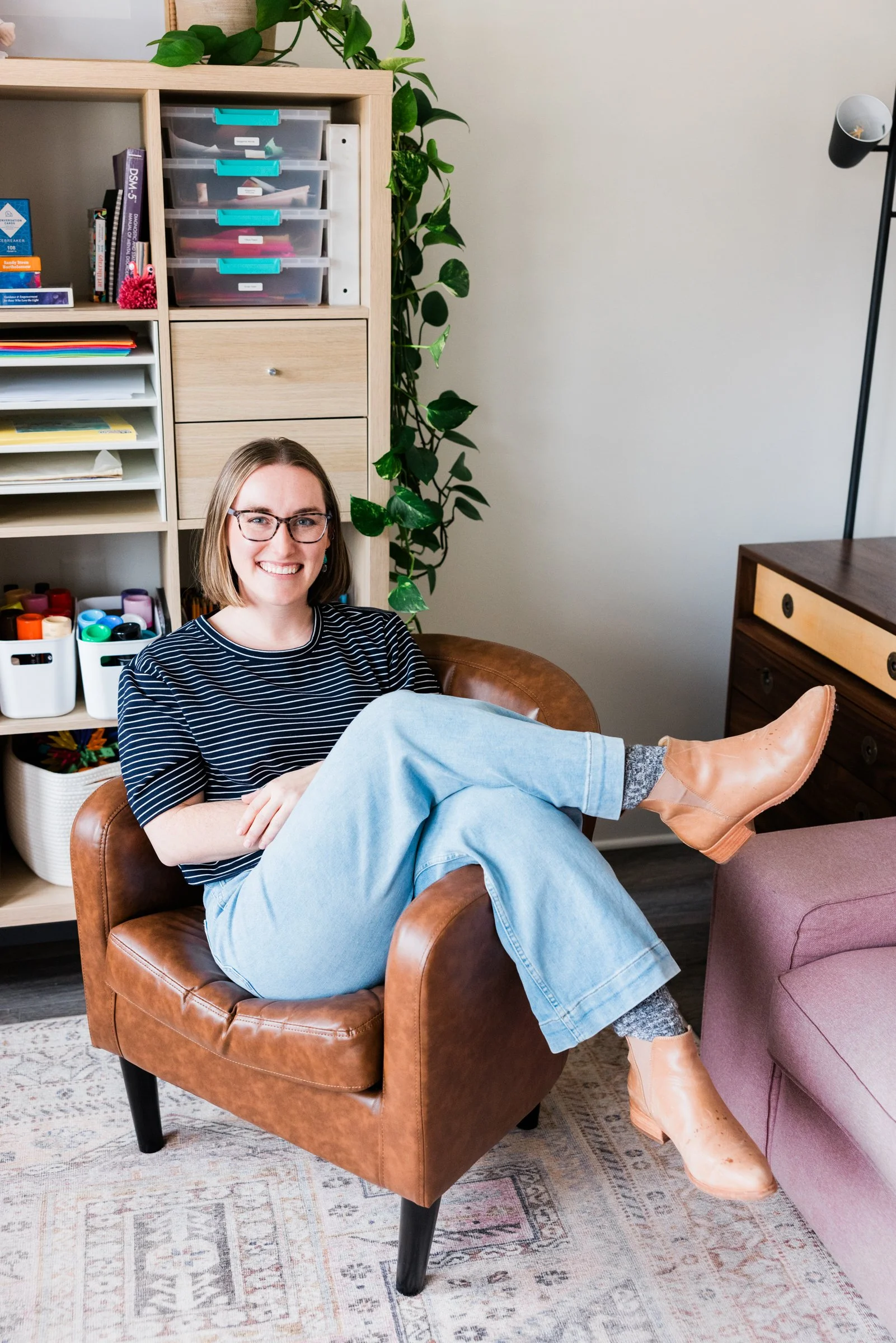 parent coaching in northern virginia. A white women in a blue striped shirt sits sideways in a brown chair.