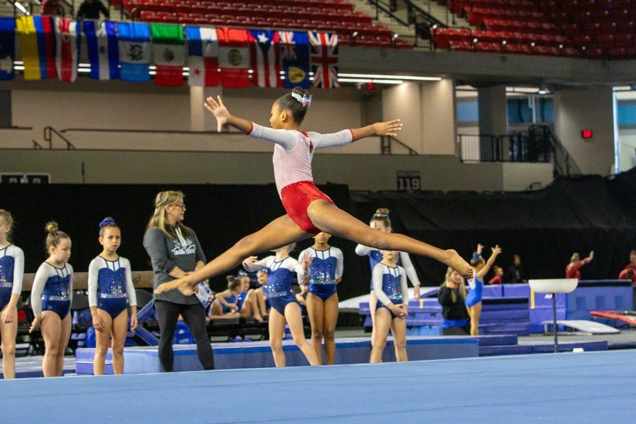 Gymnast in a white and red leotard completing a split leap mid air